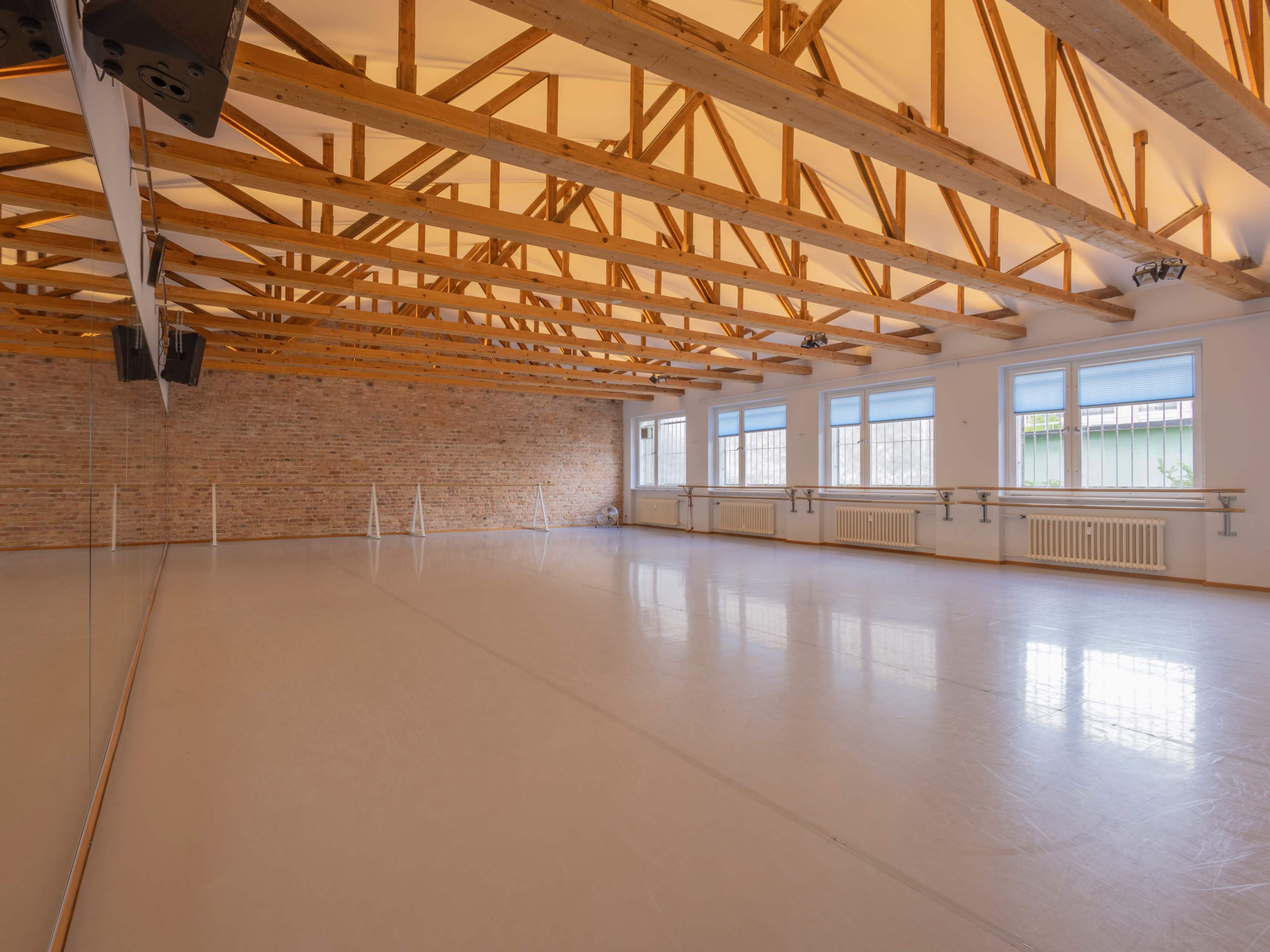 A spacious, empty dance studio with wooden beams, large windows, and a mirrored wall.
