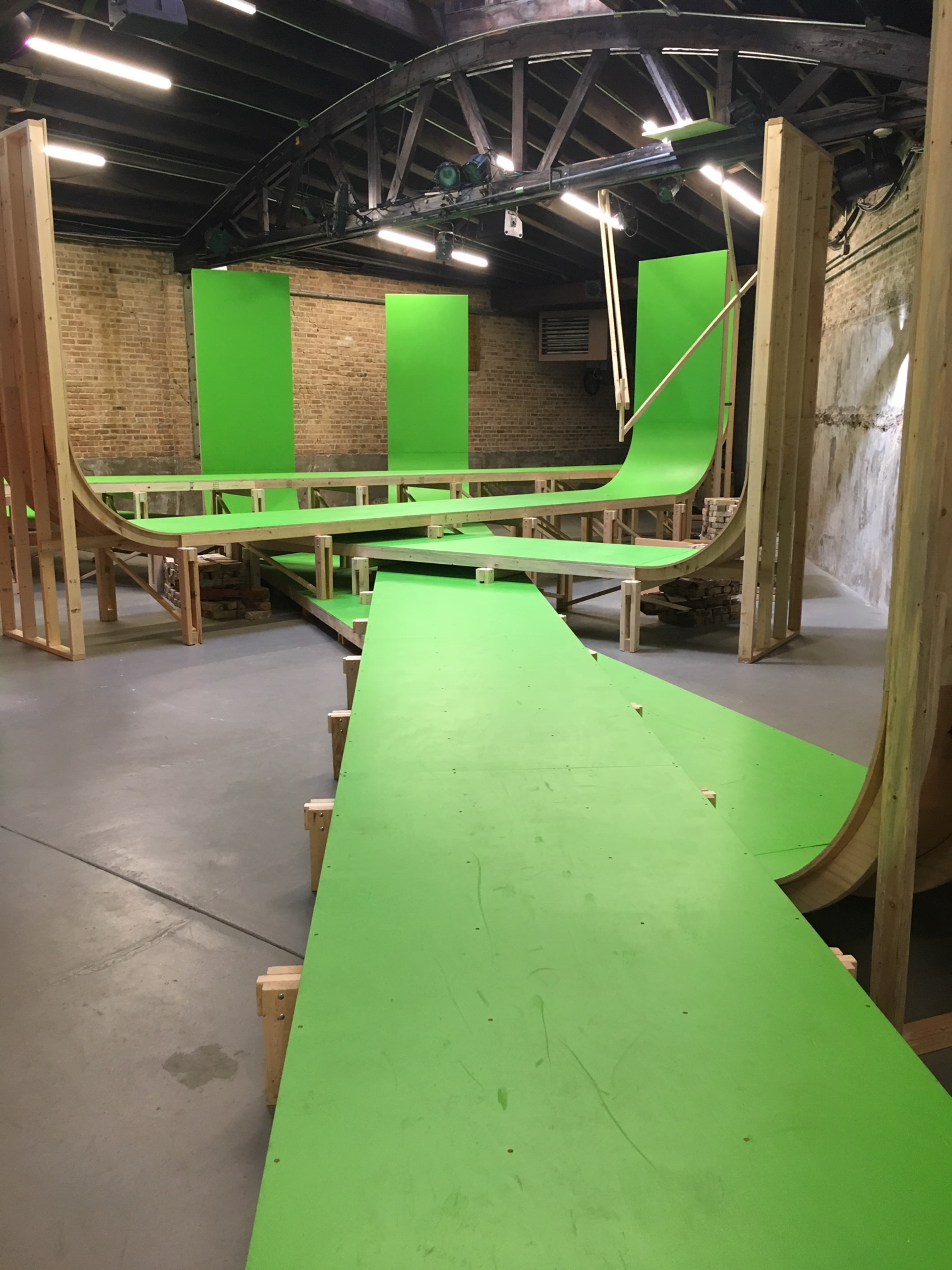 A skateboarding ramp setup with wooden frames and bright green surfaces in an indoor space.