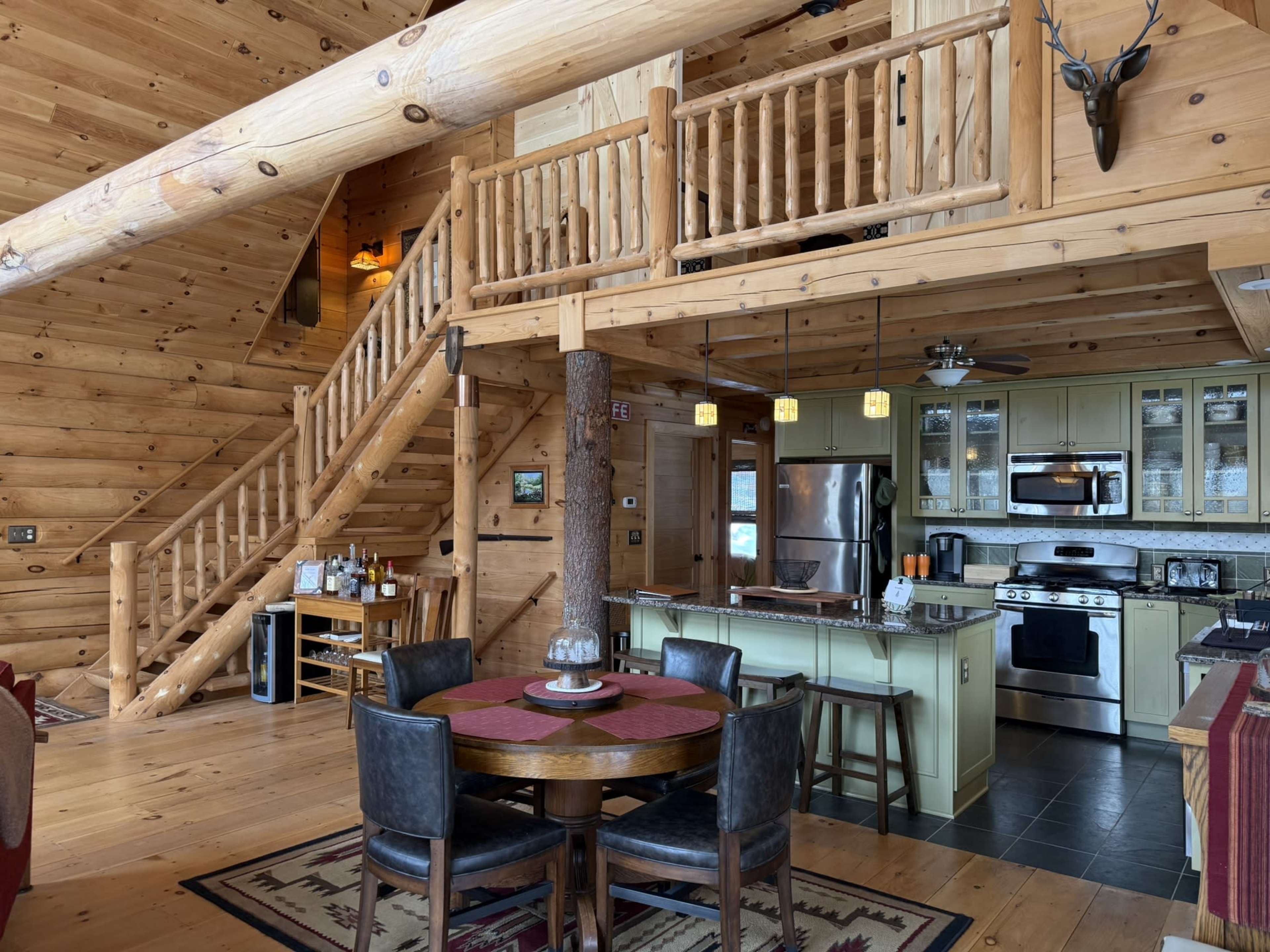 A spacious wooden cabin interior features a kitchen, dining area, and a staircase leading to a loft.