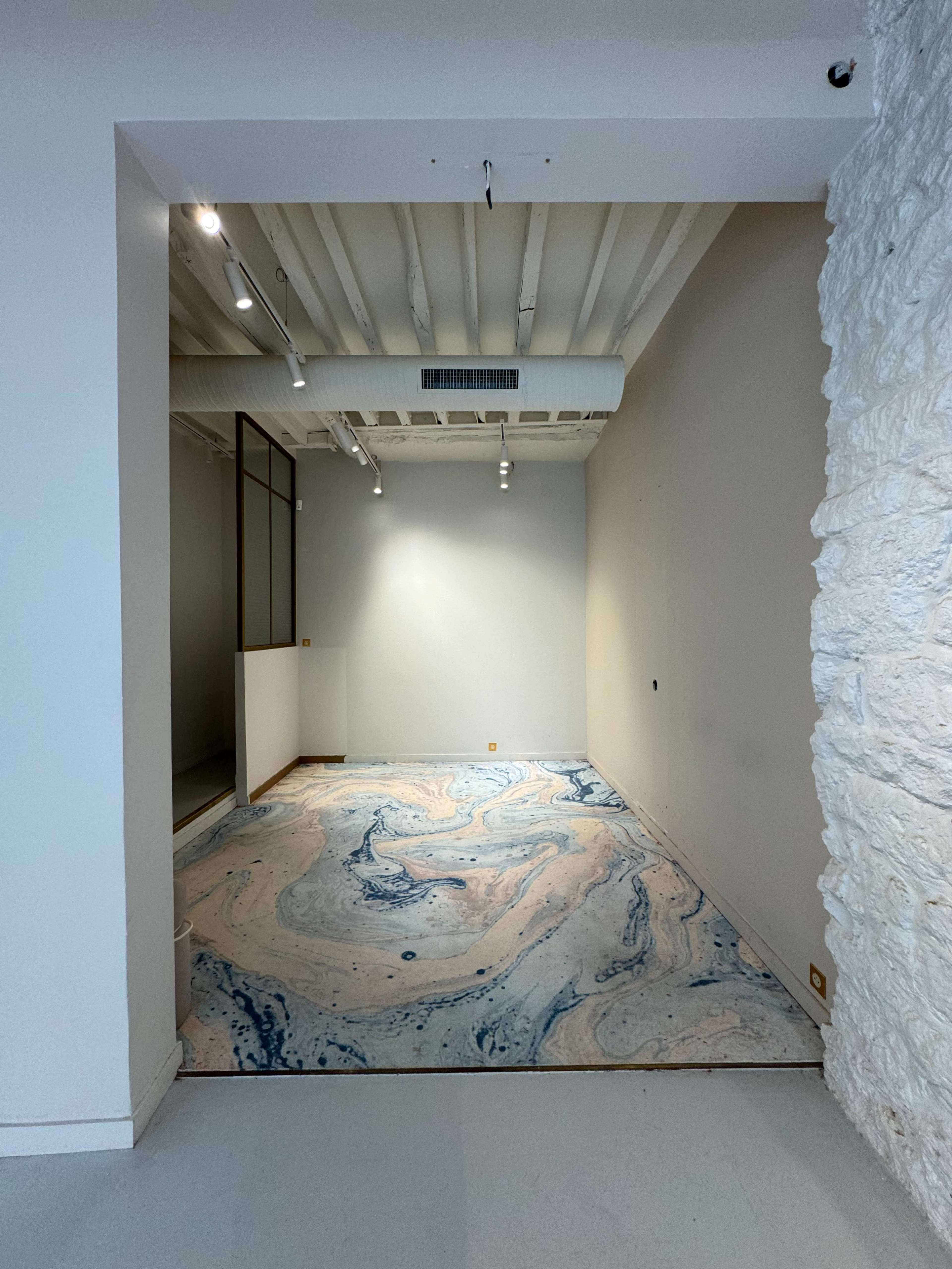 An empty room with a marbled blue and beige carpet and a textured stone wall on one side.