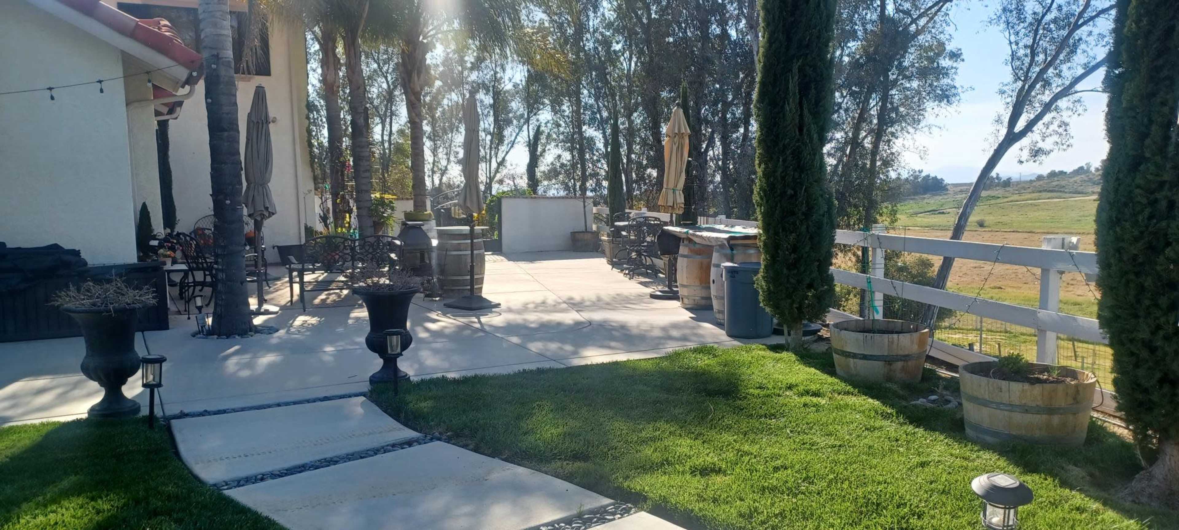 A spacious outdoor patio features seating areas, a bar, and decorative planters surrounded by trees and open fields.