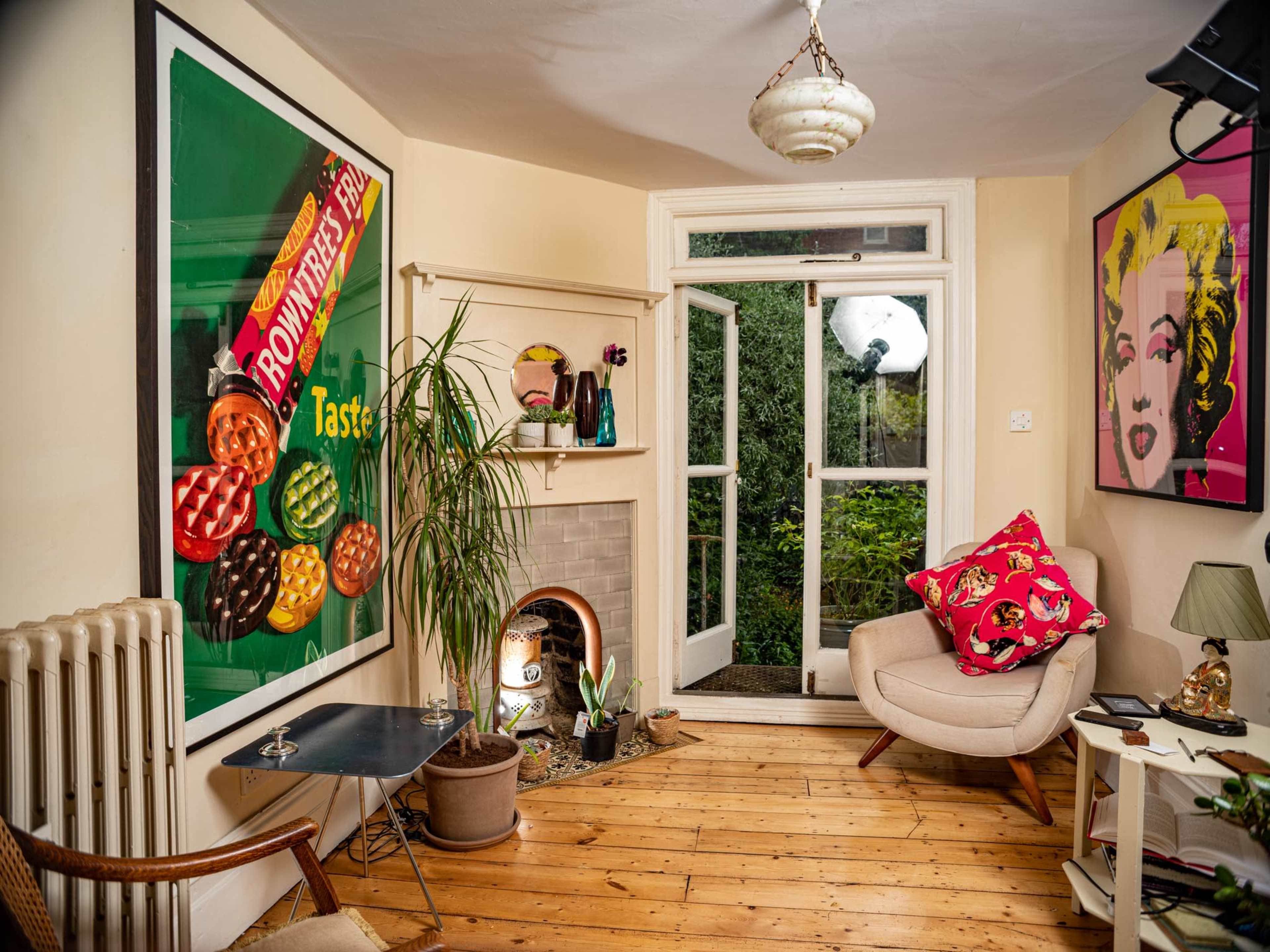 A cozy living room featuring colorful artwork on the walls, a small fireplace, and a door opening to a garden.