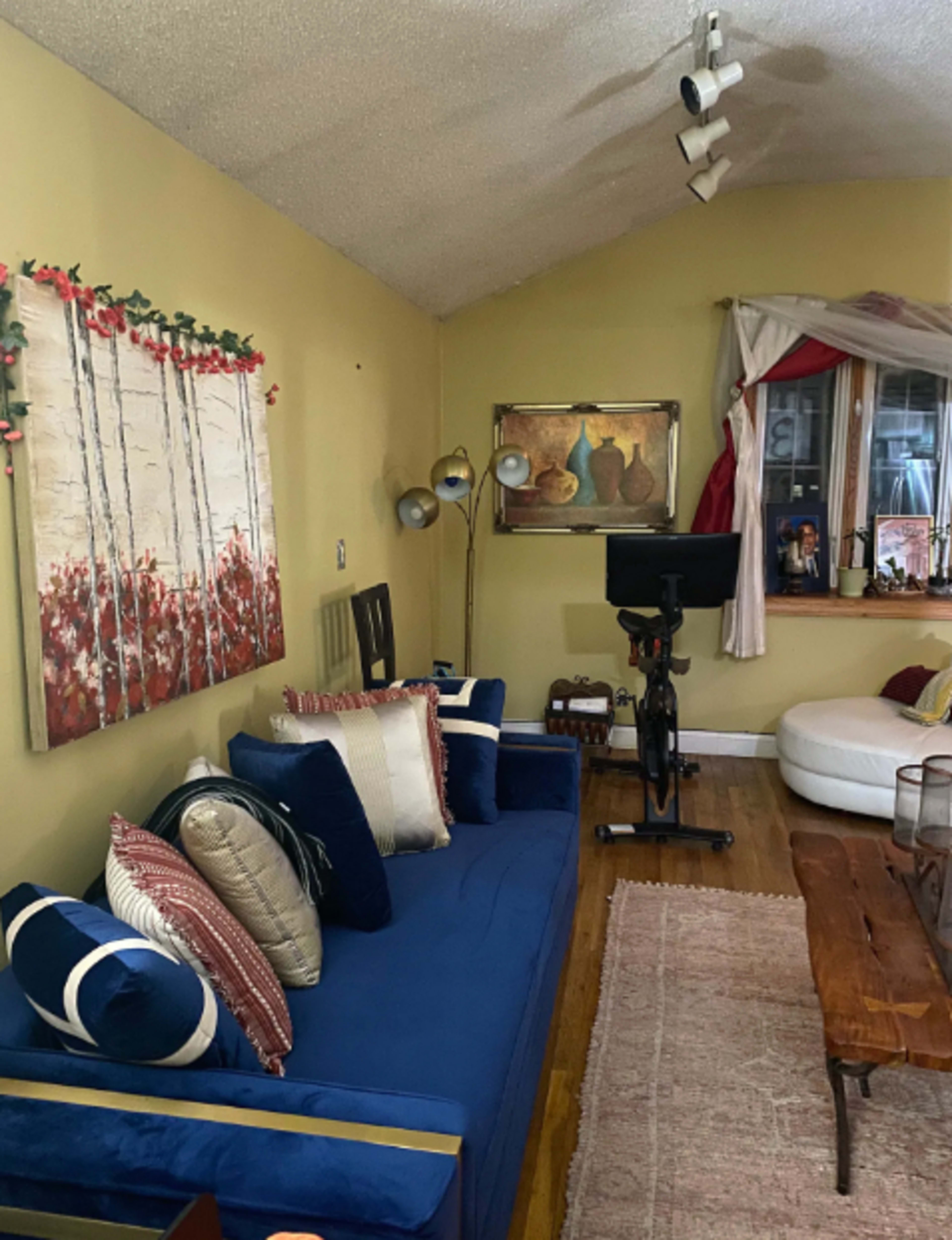 A cozy living room with a blue sofa adorned with decorative pillows, a wooden coffee table, and a large window featuring natural light.