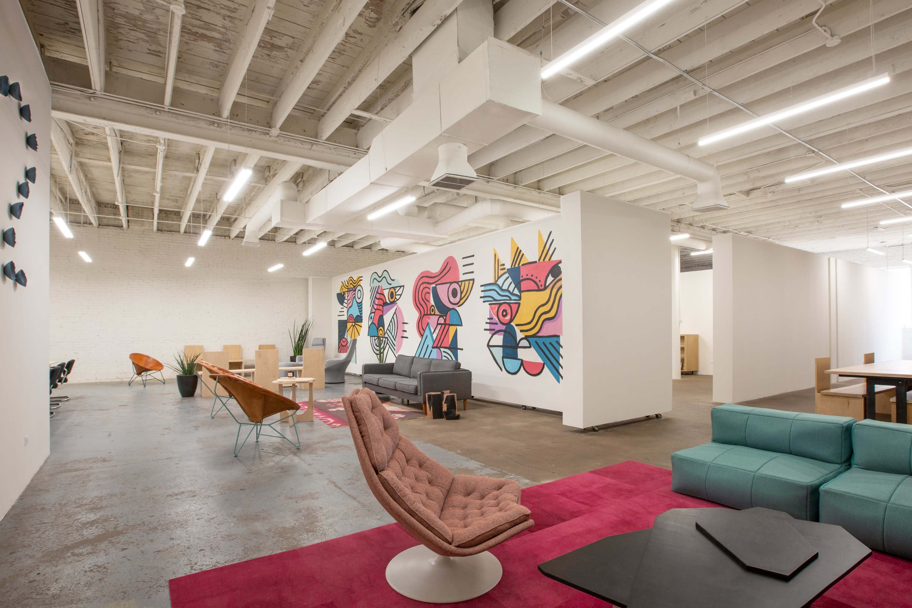 A modern office interior featuring colorful murals, various seating arrangements, and an open layout with concrete floors and exposed beams.