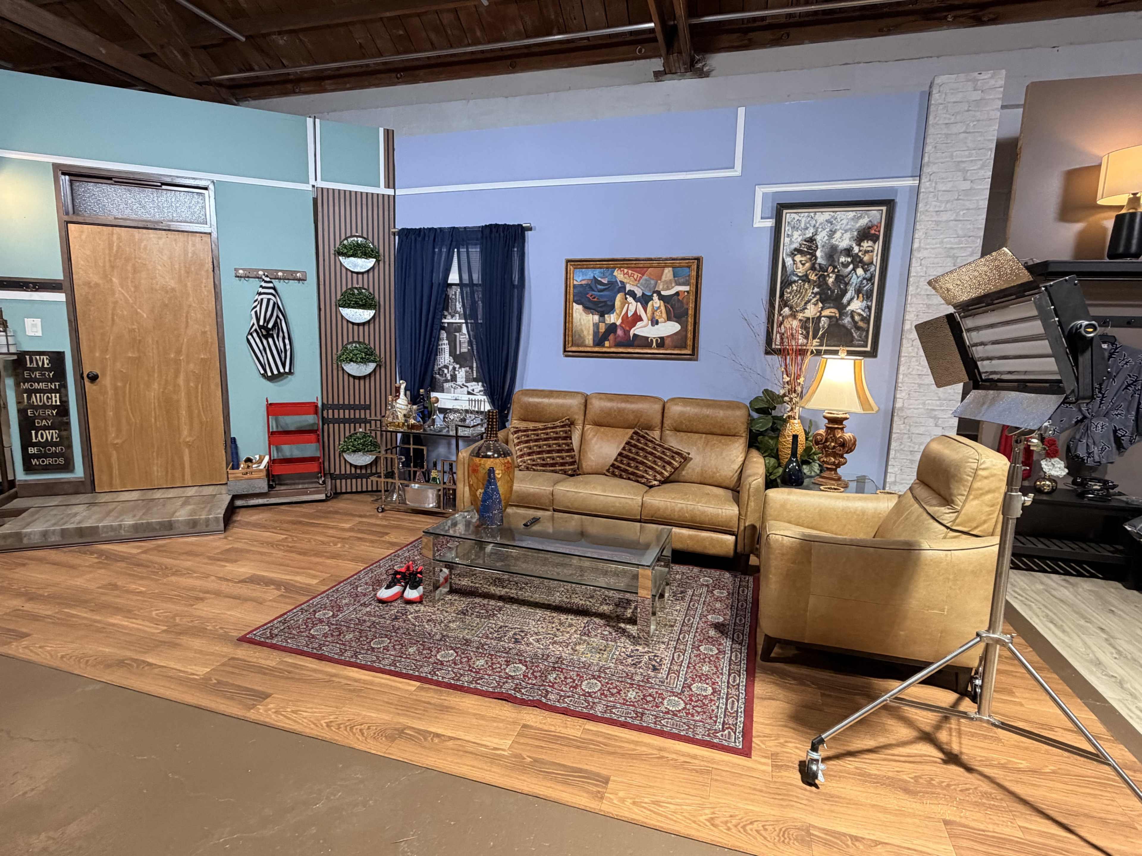 The image shows a staged living room scene with a beige couch, decorative art on the walls, a glass coffee table on a patterned rug, and various decorative items around the space.
