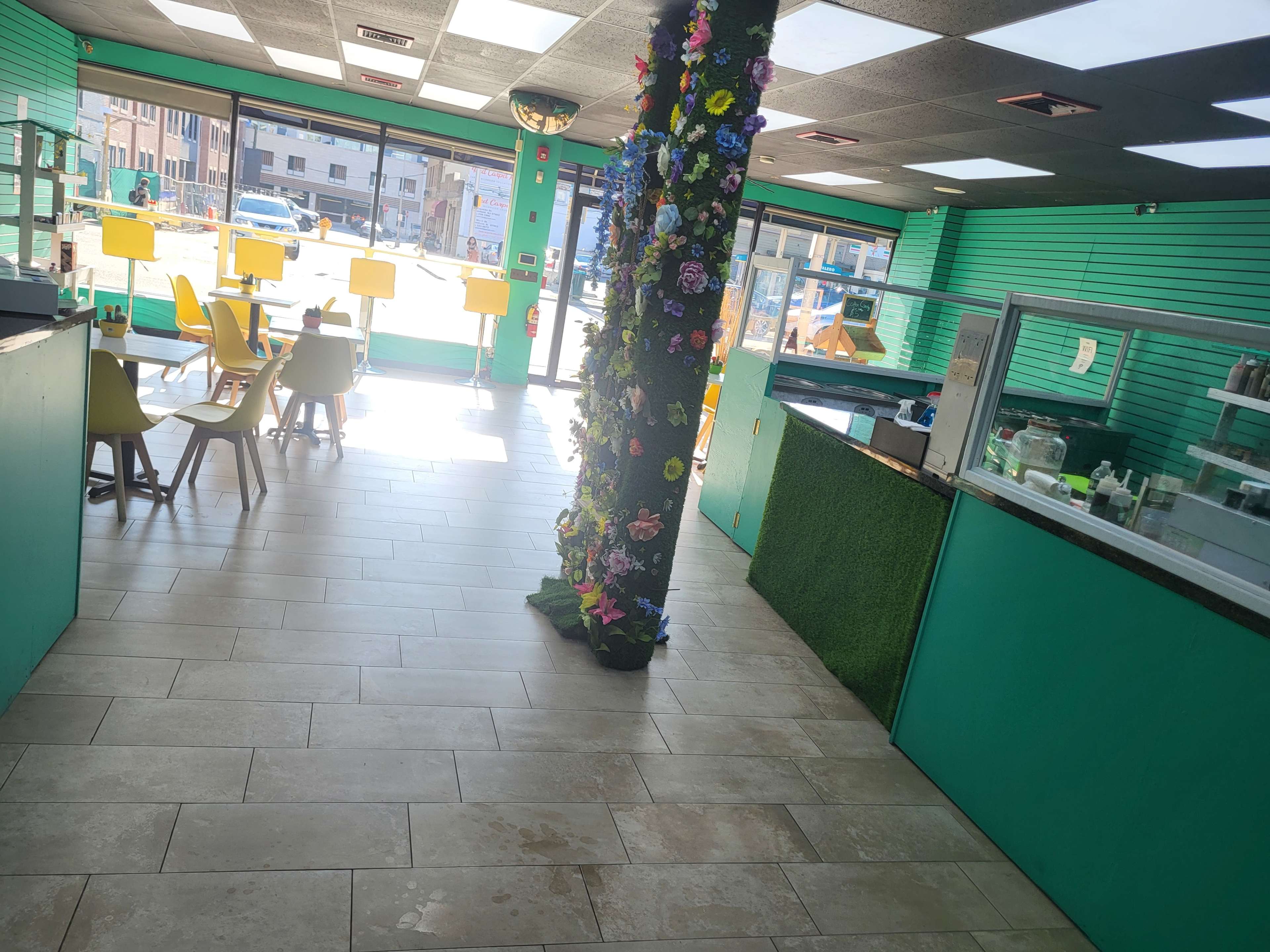 A brightly colored interior of a café or shop with green walls, a floral column, and seating arrangements including yellow chairs and tables.