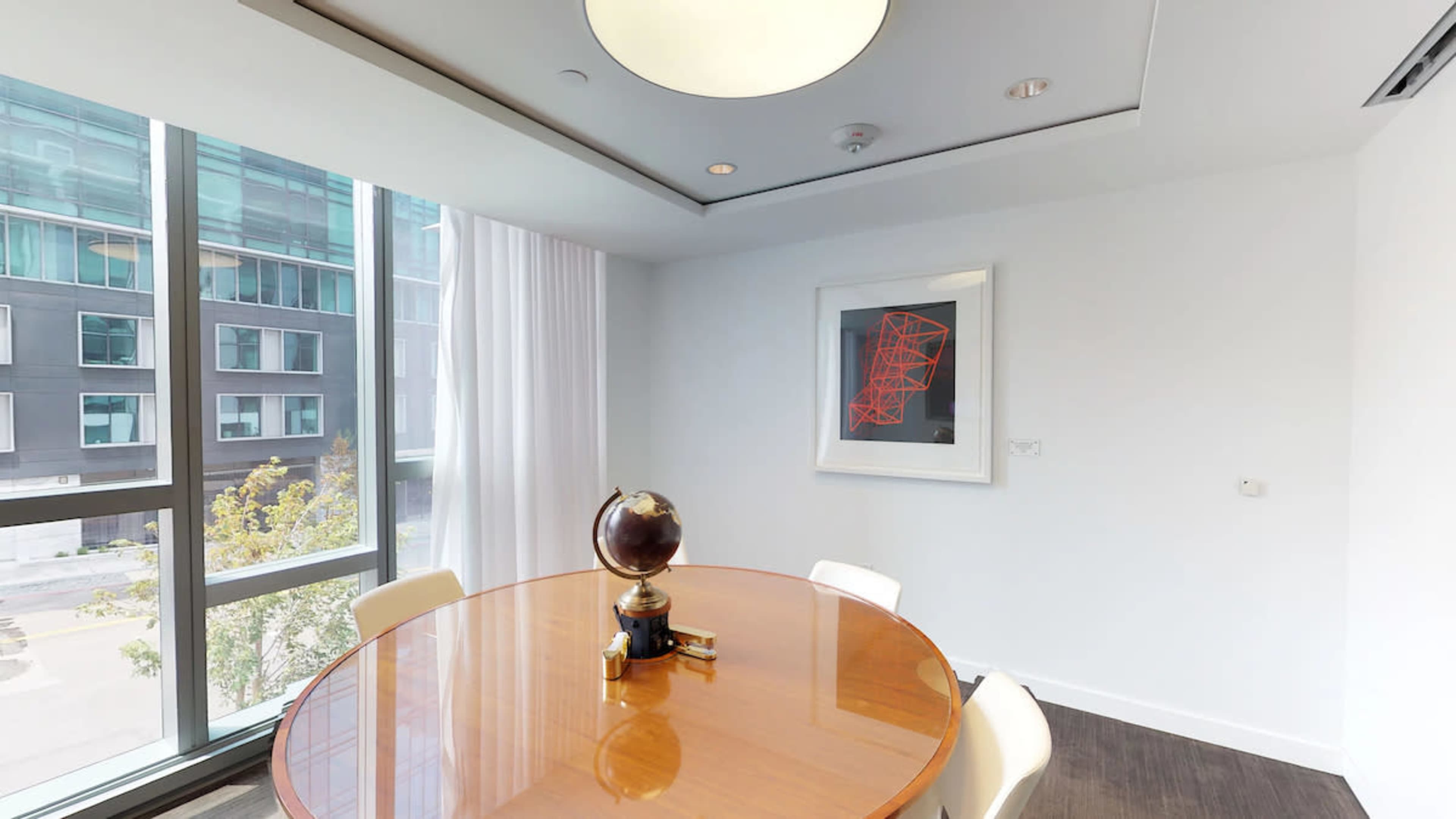 A round wooden table with a globe centerpiece is positioned near large windows in a modern office space.