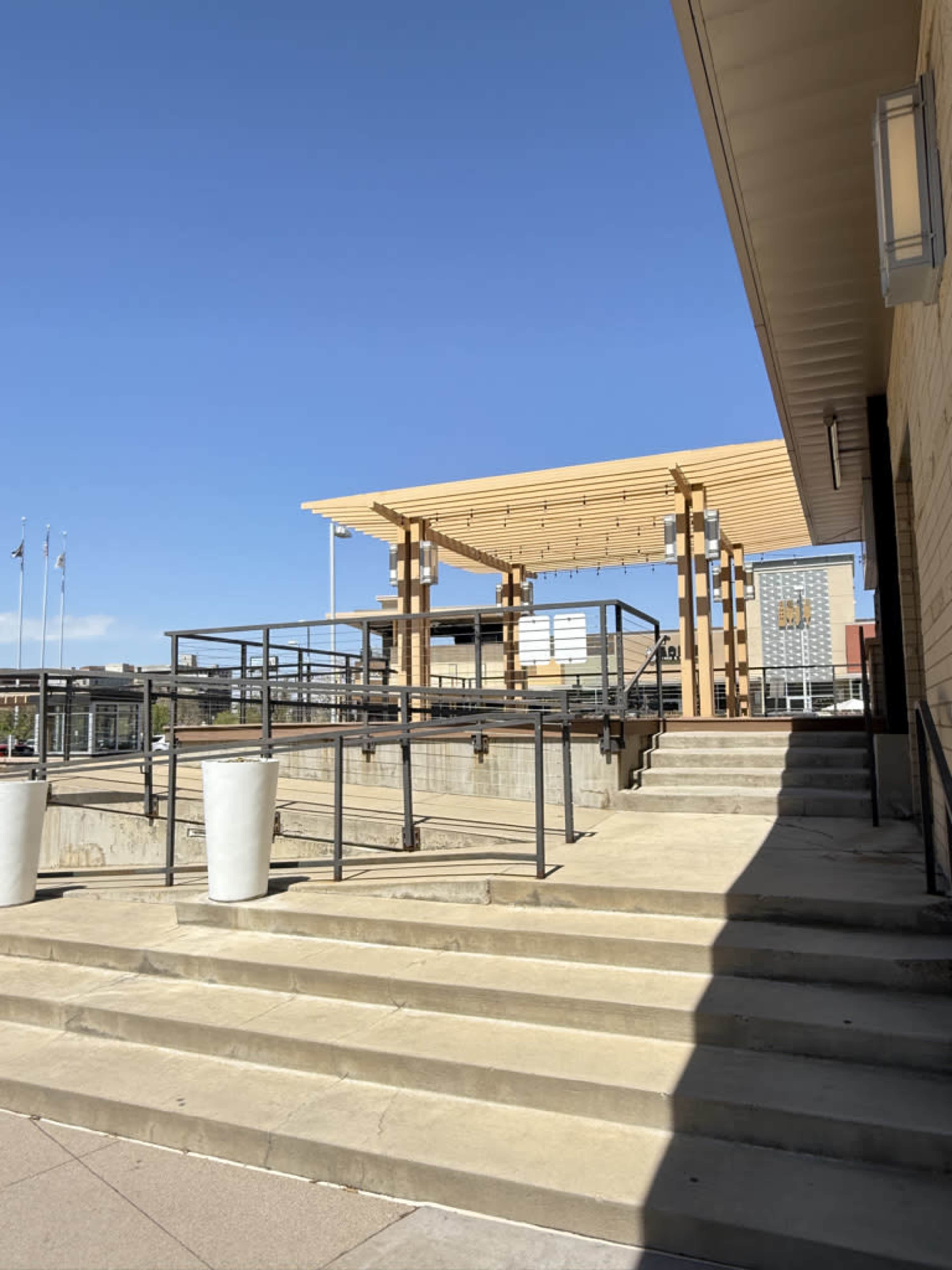 A large wooden structure with a slatted roof is situated on a concrete platform, with metal railings and steps leading up to it.