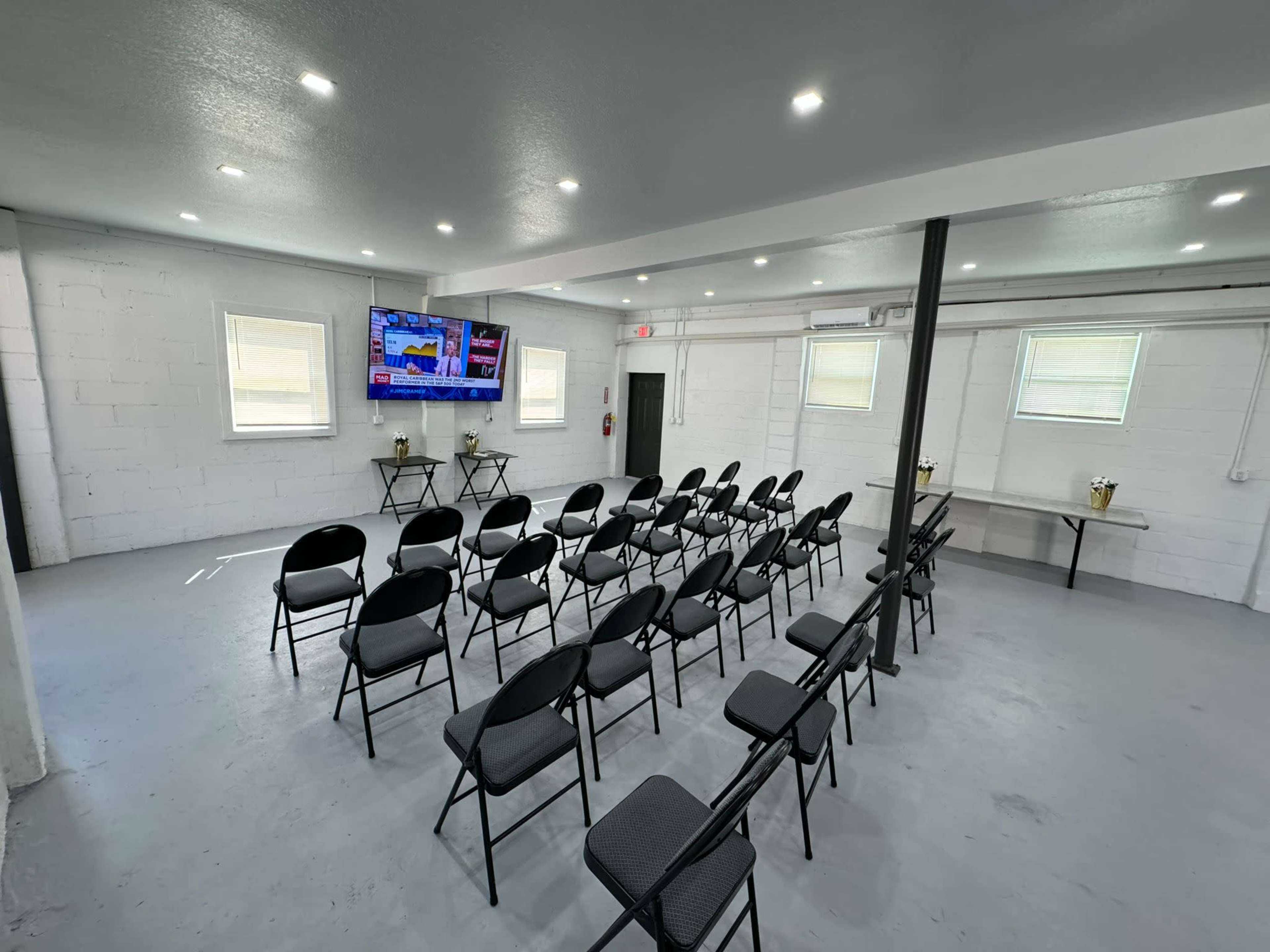 A modern meeting room set up with rows of black chairs facing a large television screen mounted on the wall.