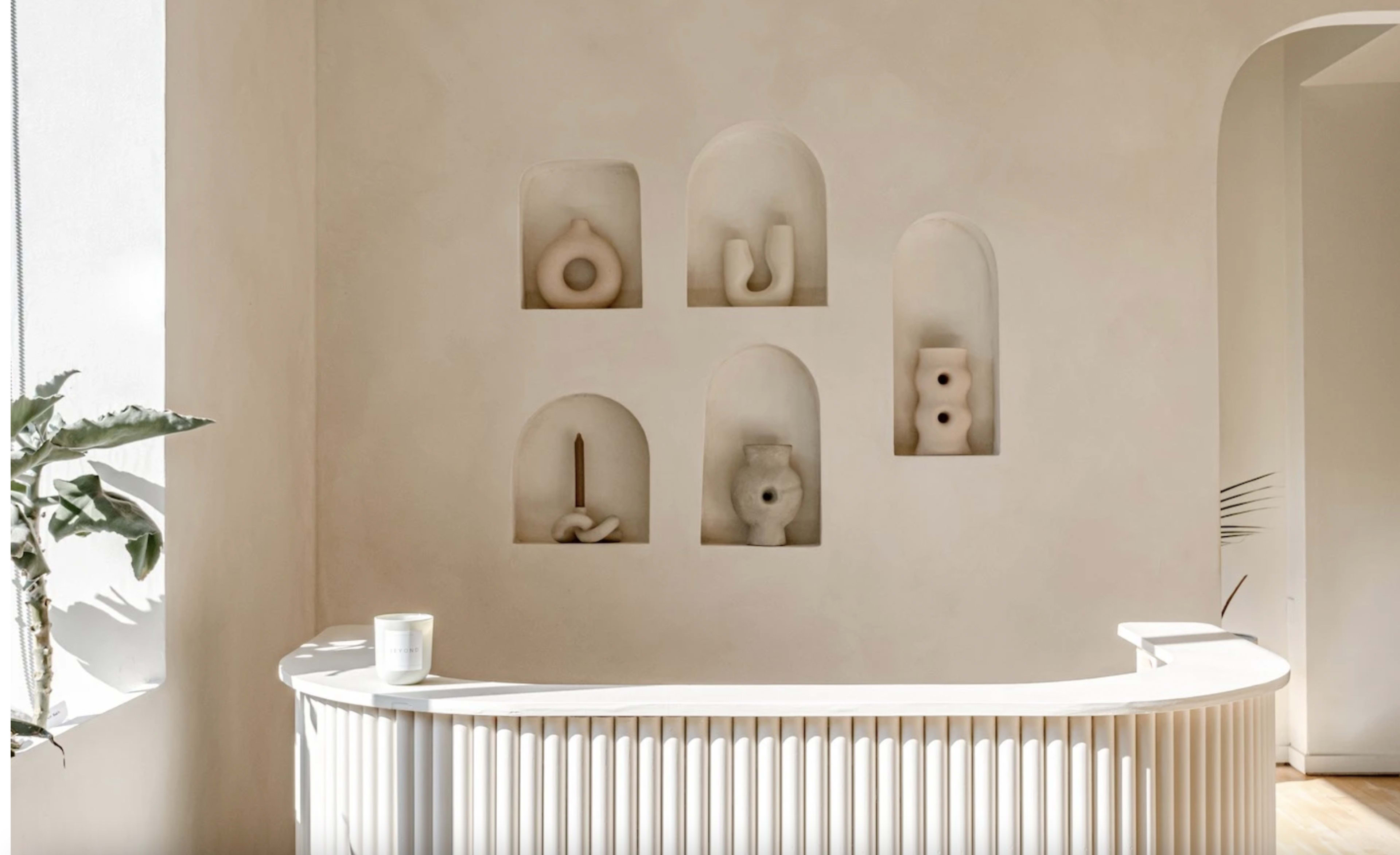 A modern reception area with a curved white counter and six sculptural pieces displayed in recessed alcoves on the wall.