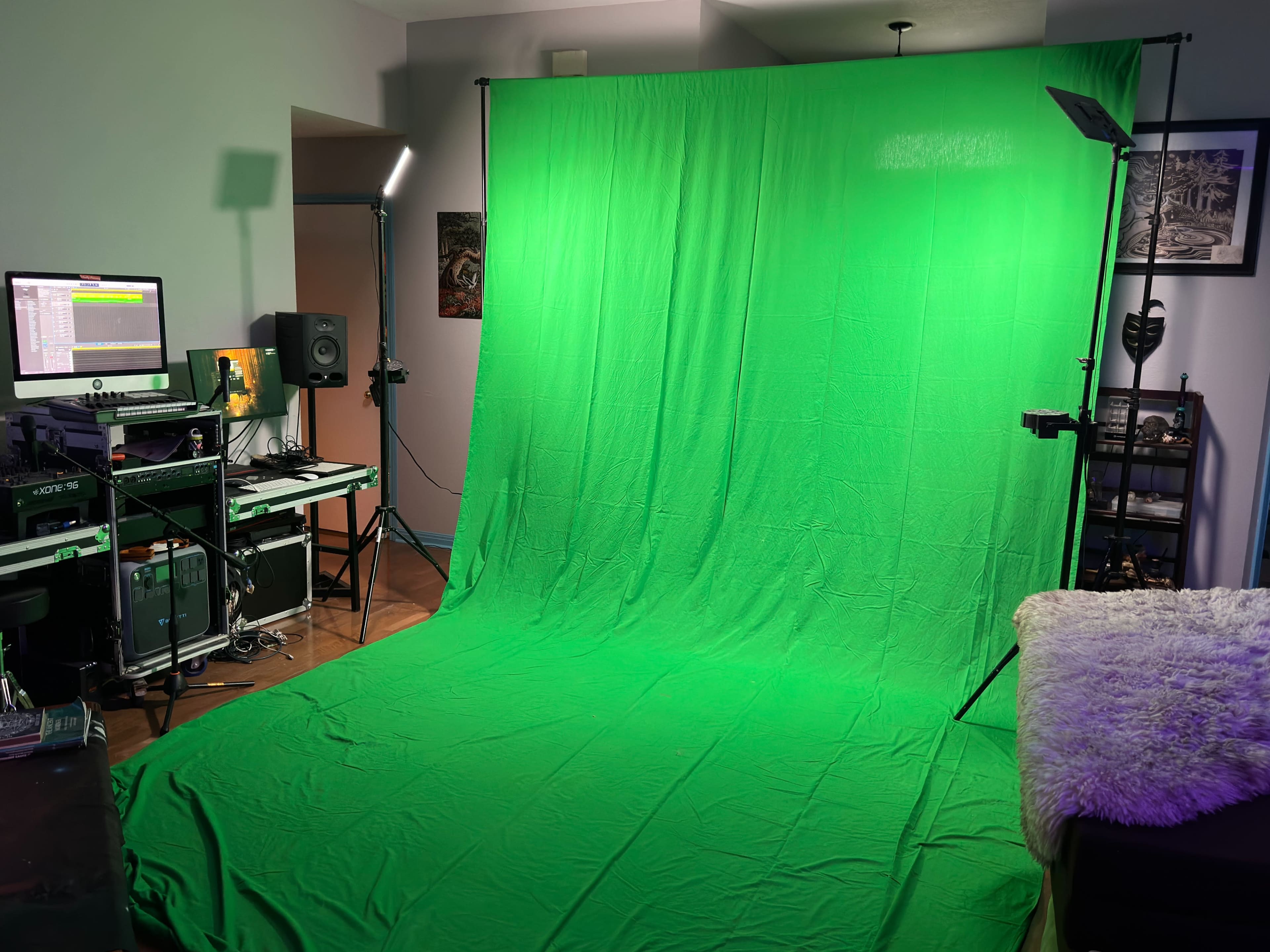 The image shows a room with a large green backdrop setup, accompanied by audio equipment and a computer station.