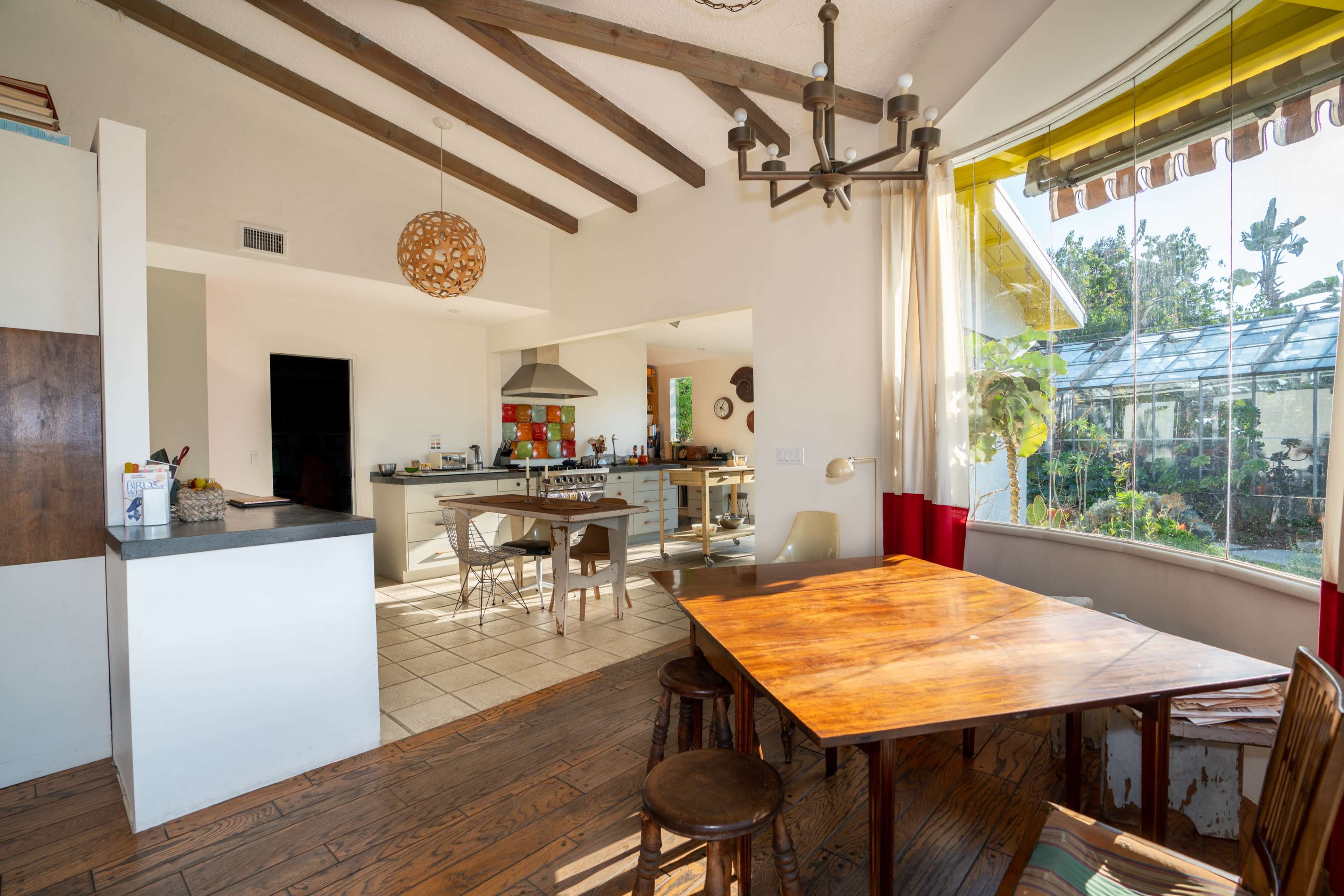 A modern kitchen and dining area with wooden beams, a table, and large windows revealing a garden outside.