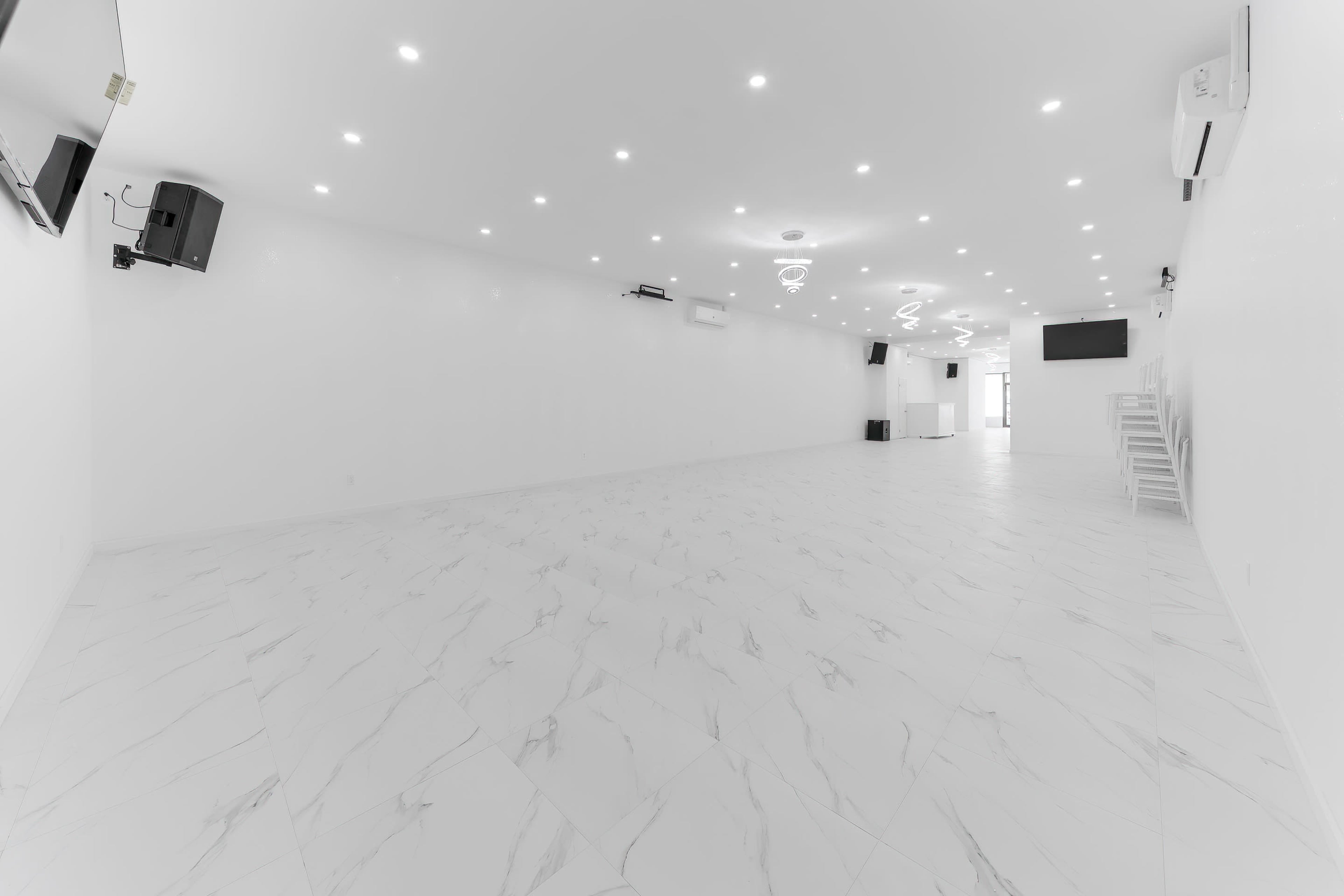 A spacious, empty room with white walls, a tiled floor, and modern lighting fixtures.
