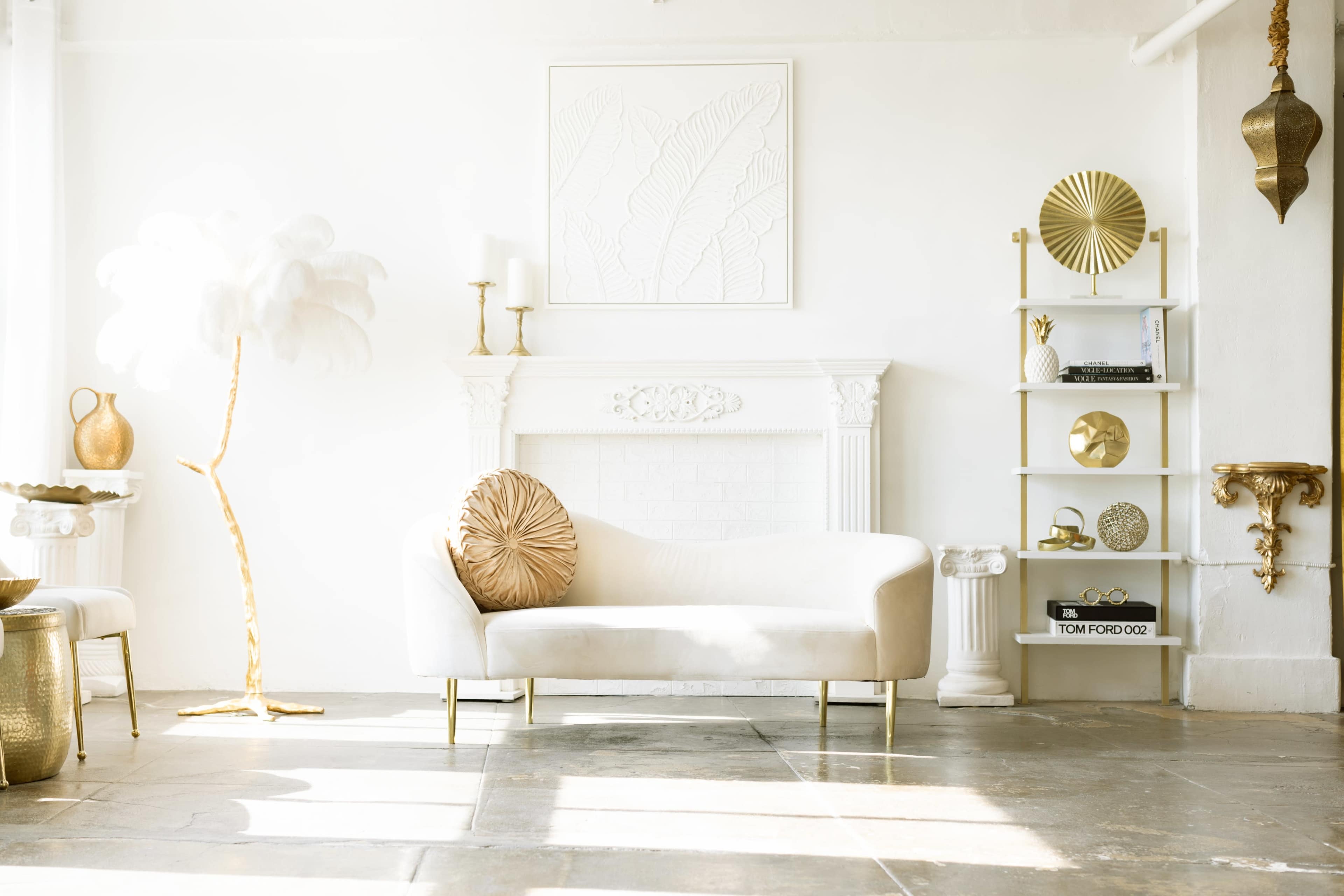 The scene features a bright, minimalist living room with a light-colored sofa, a decorative palm tree, and a shelf displaying various decorative items against a white wall.