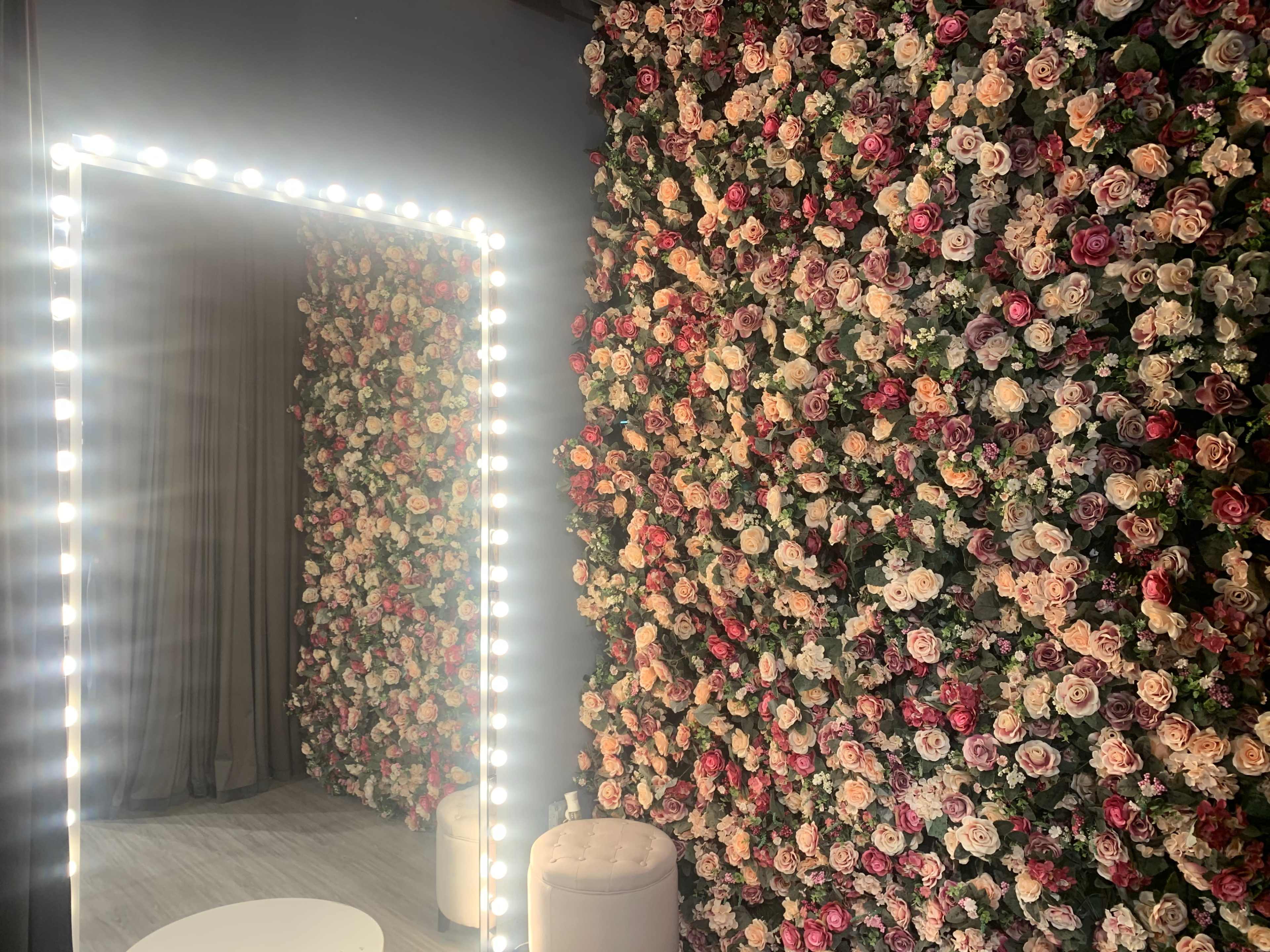 A room with two flower-covered walls and an illuminated mirror framed by bright lights.
