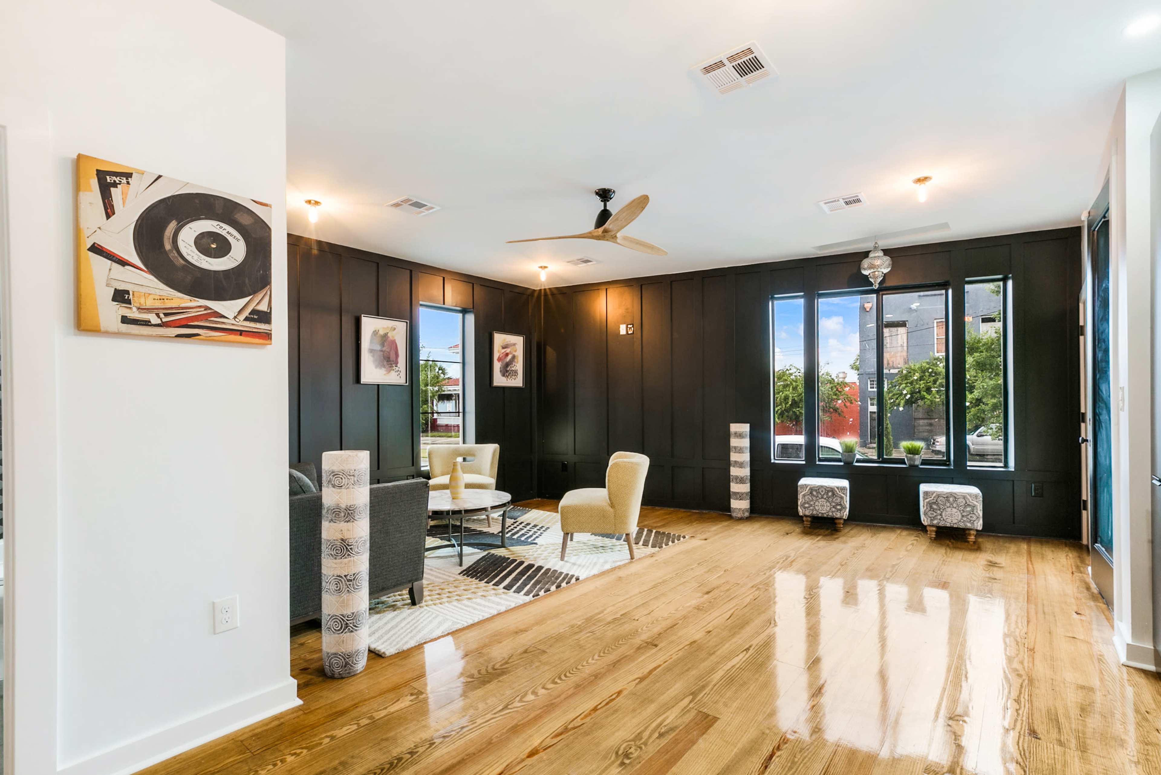 A stylish living room with dark-paneled walls, wooden flooring, and large windows allowing natural light.