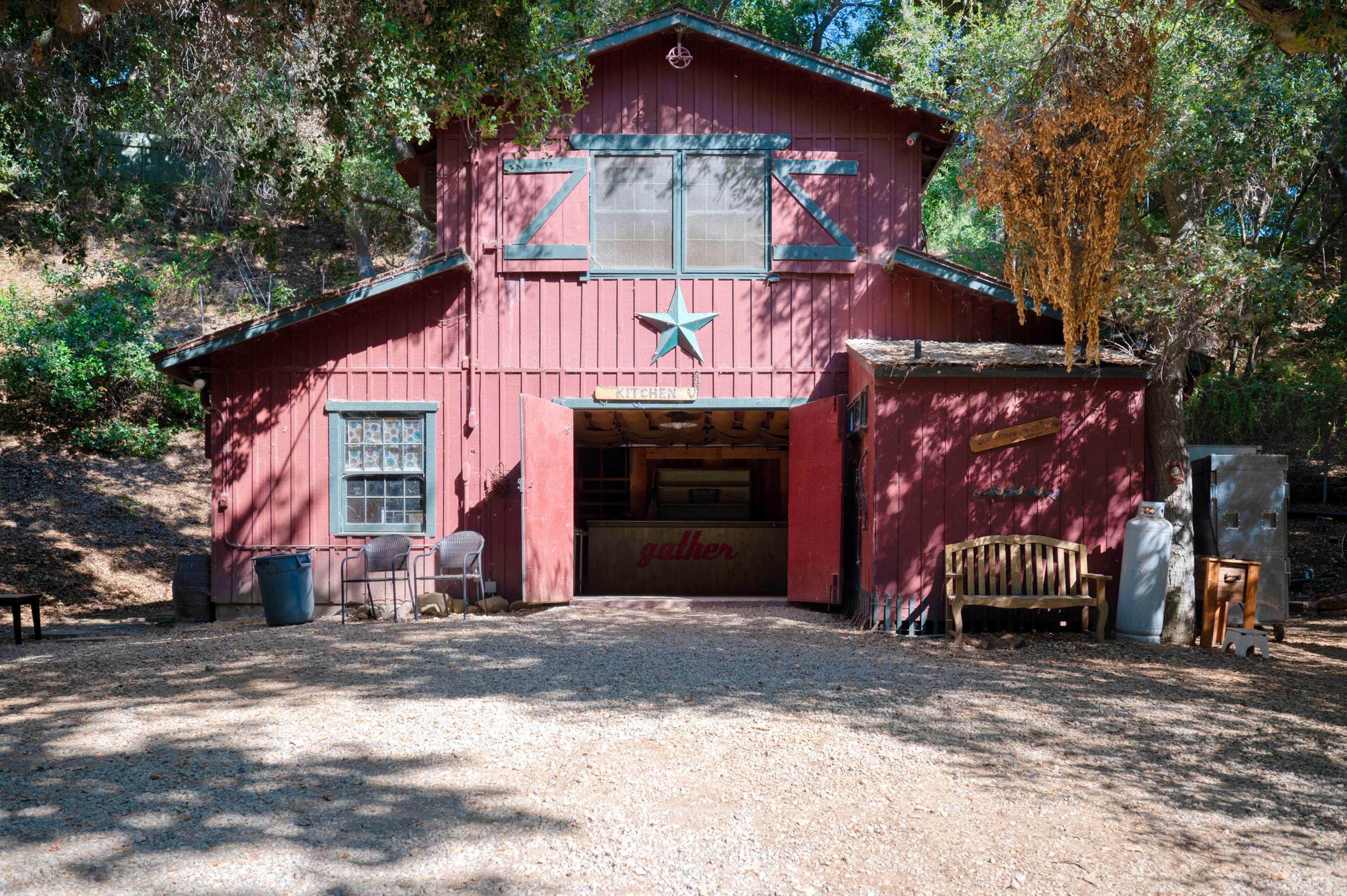 A red barn with a green star on the front is situated among trees, with a gravel path leading to it.