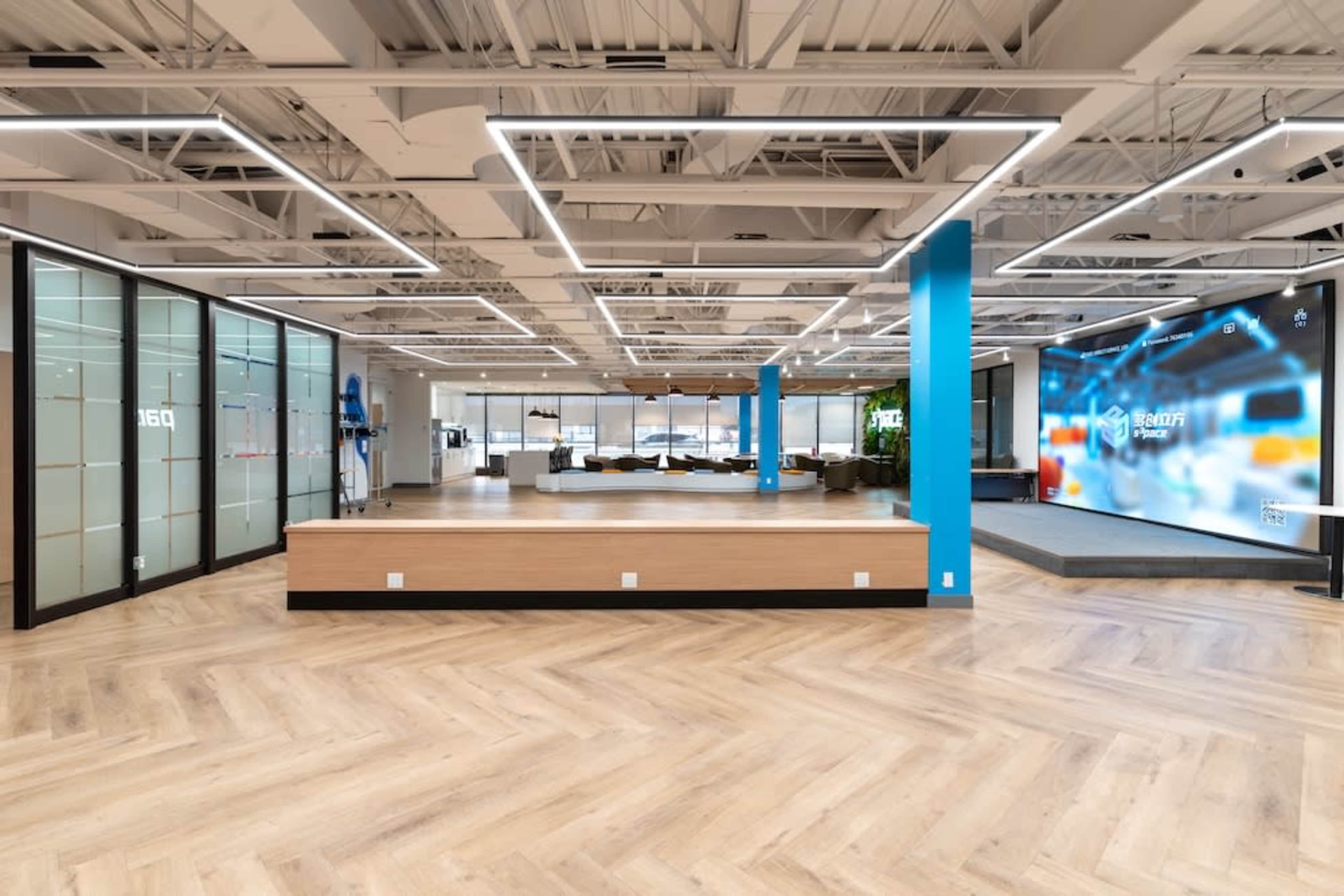 An open office space features modern design elements with wooden flooring, large windows, and a blue accent wall.
