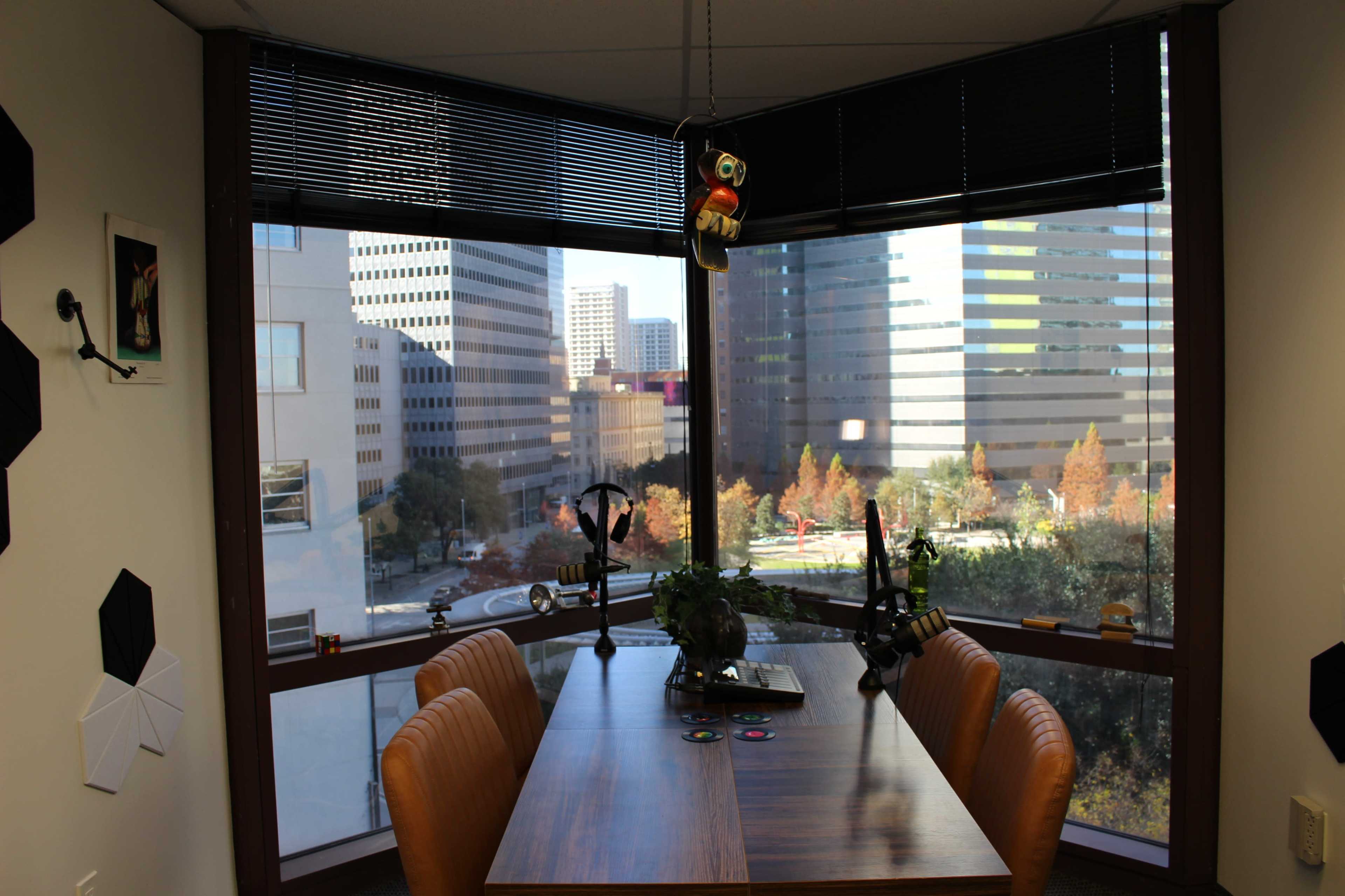 The image shows a modern office space with a wooden table and orange chairs, overlooking a cityscape through large windows.