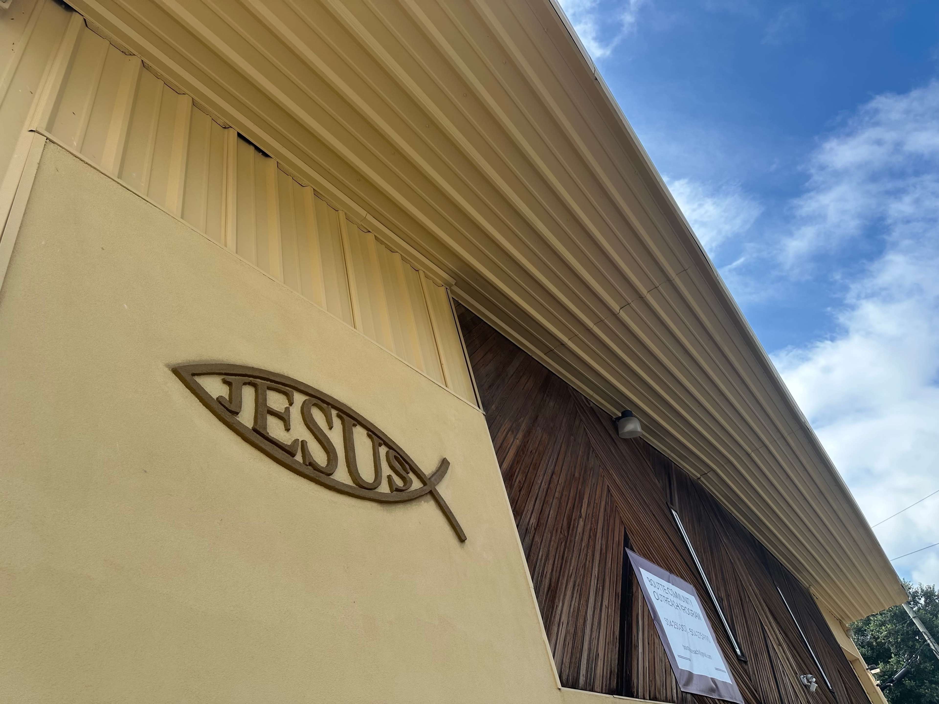 A fish symbol and the word "JESUS" are displayed on the exterior wall of a building under a clear blue sky.