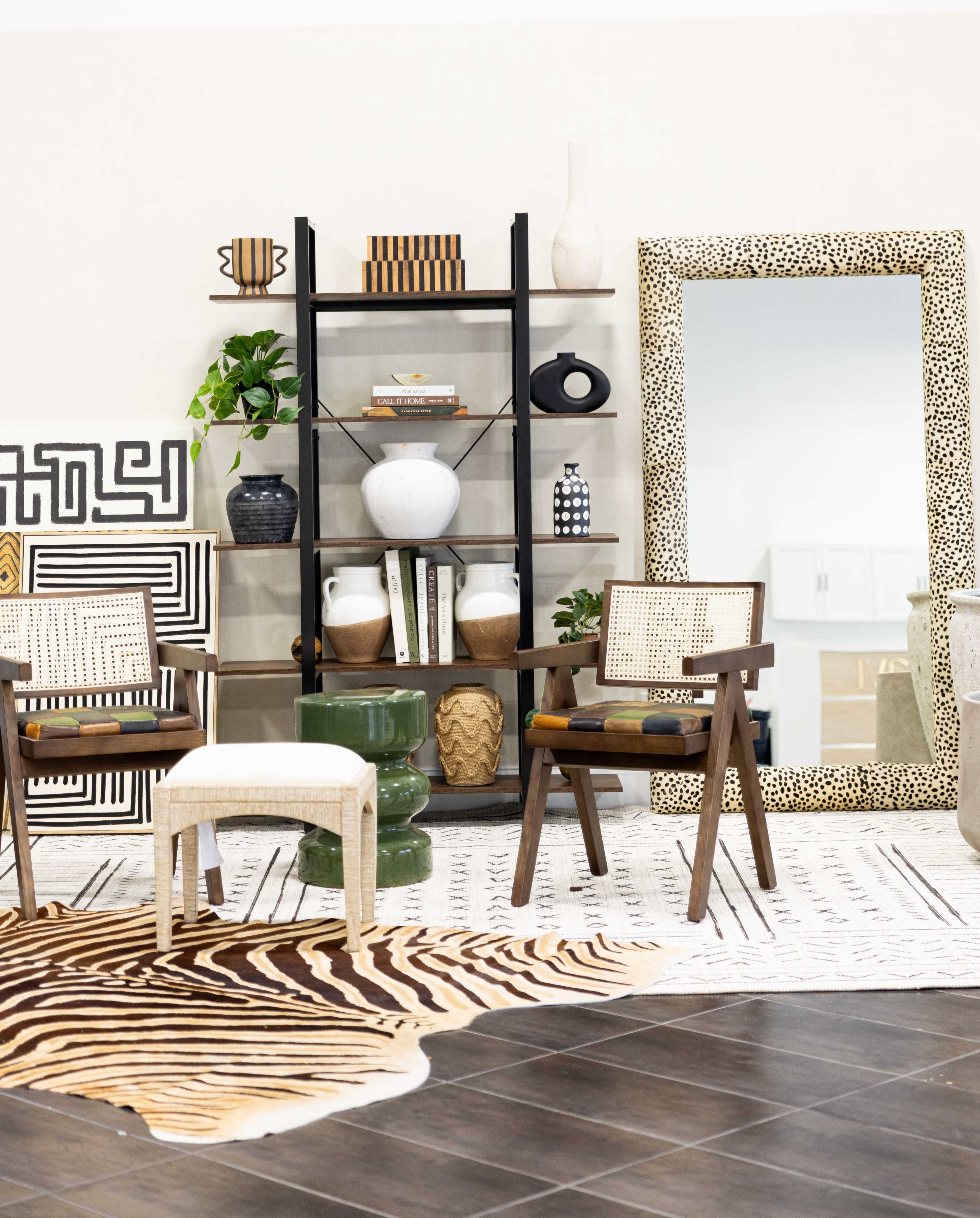 The image shows a modern living space with shelves, decorative objects, chairs, a large mirror, and patterned rugs arranged in a stylish layout.