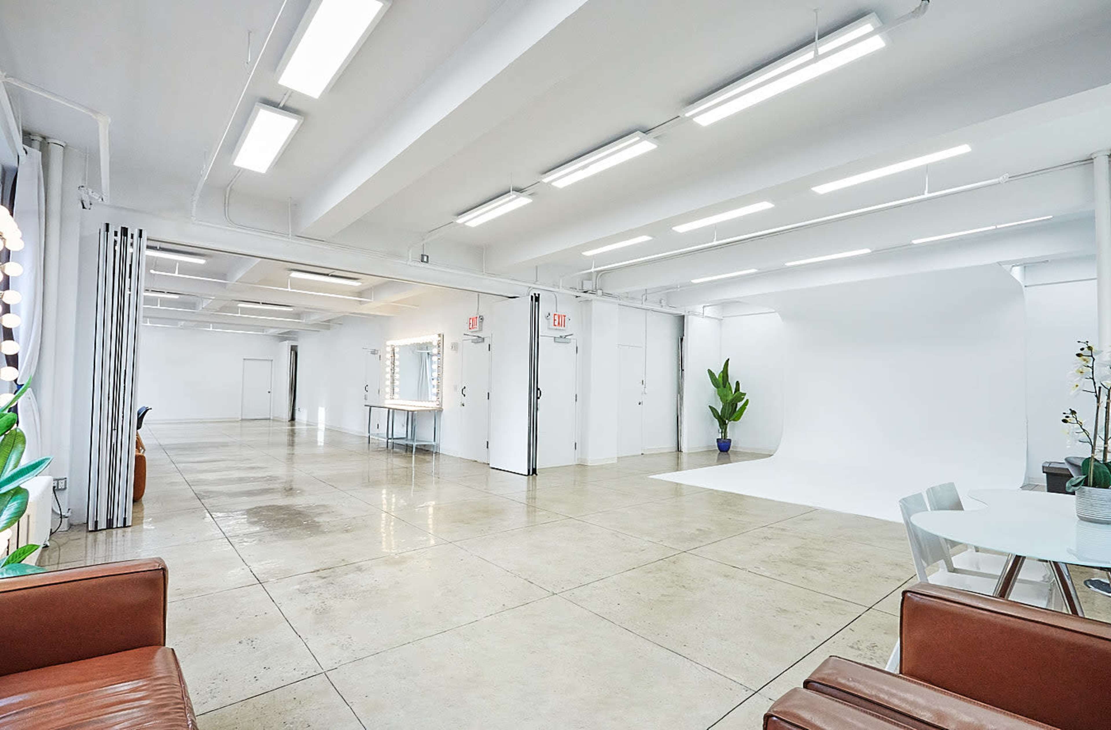 The image shows a spacious, well-lit studio with concrete flooring, a white backdrop, and seating areas.