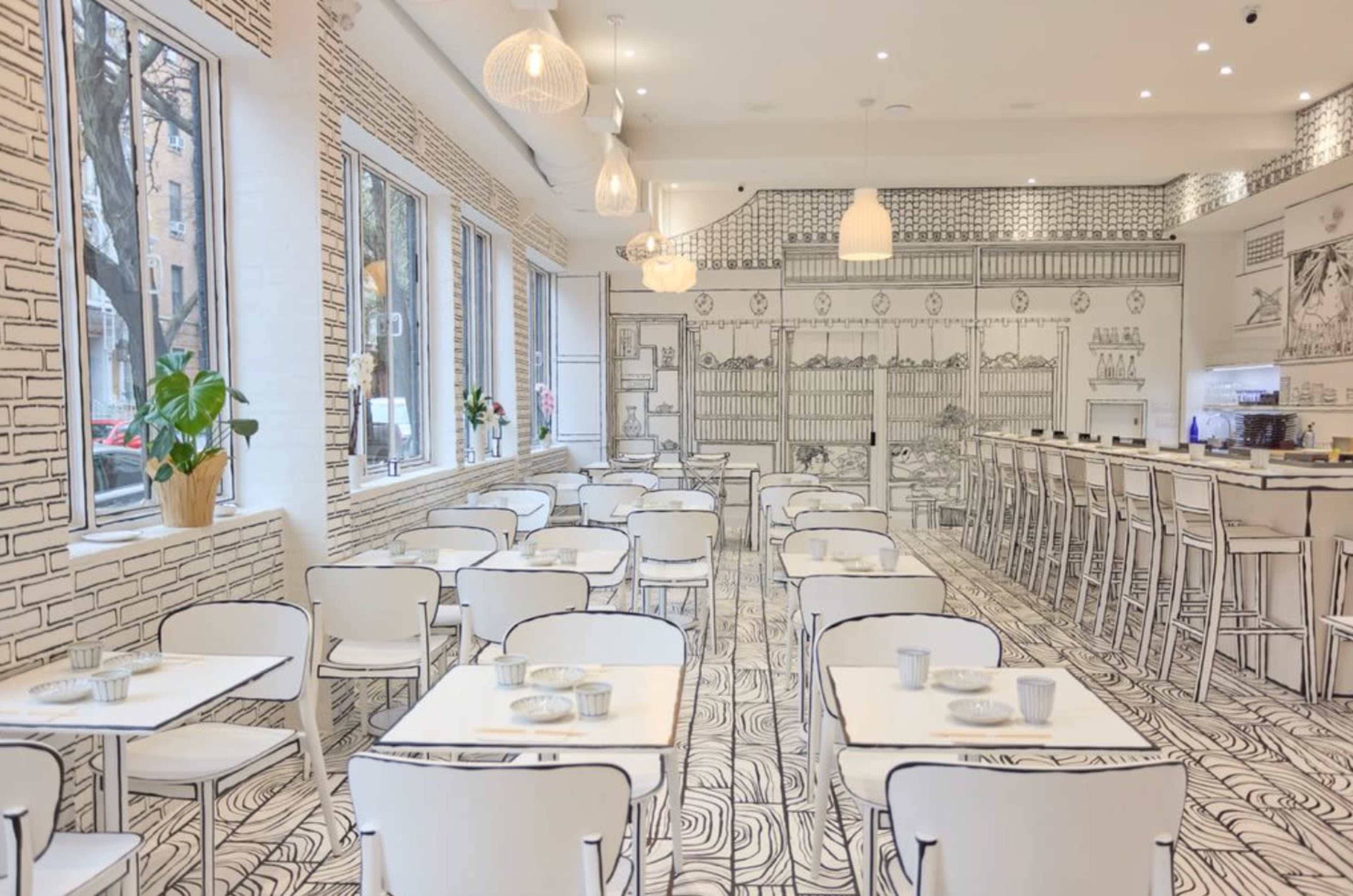 The image shows a modern café interior with white tables and chairs, featuring artistic wall decorations in a monochrome design.