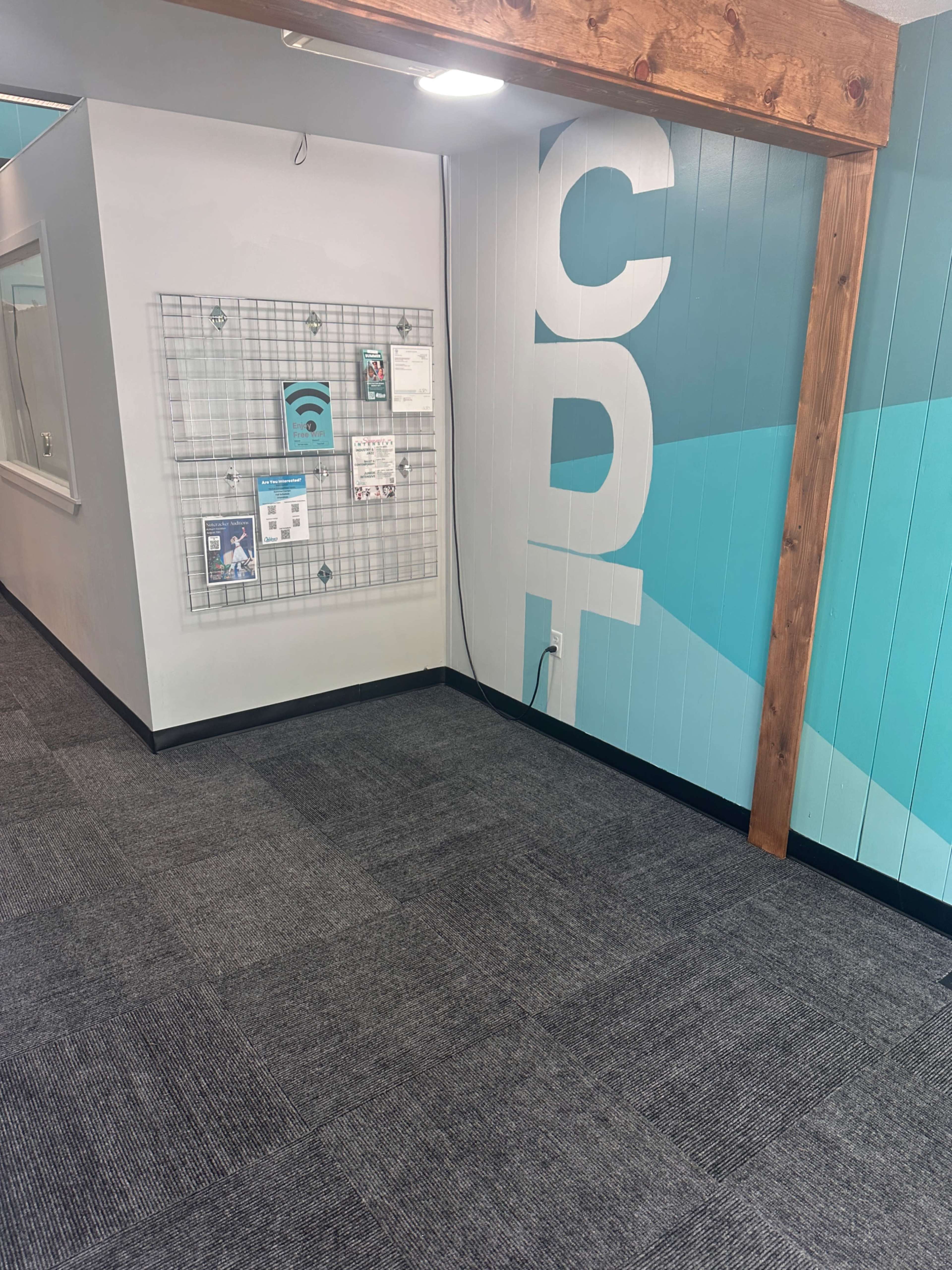 The image shows a hallway with a grid display board on the wall and the letters "CDT" painted in large font, alongside a blue and white wall design.