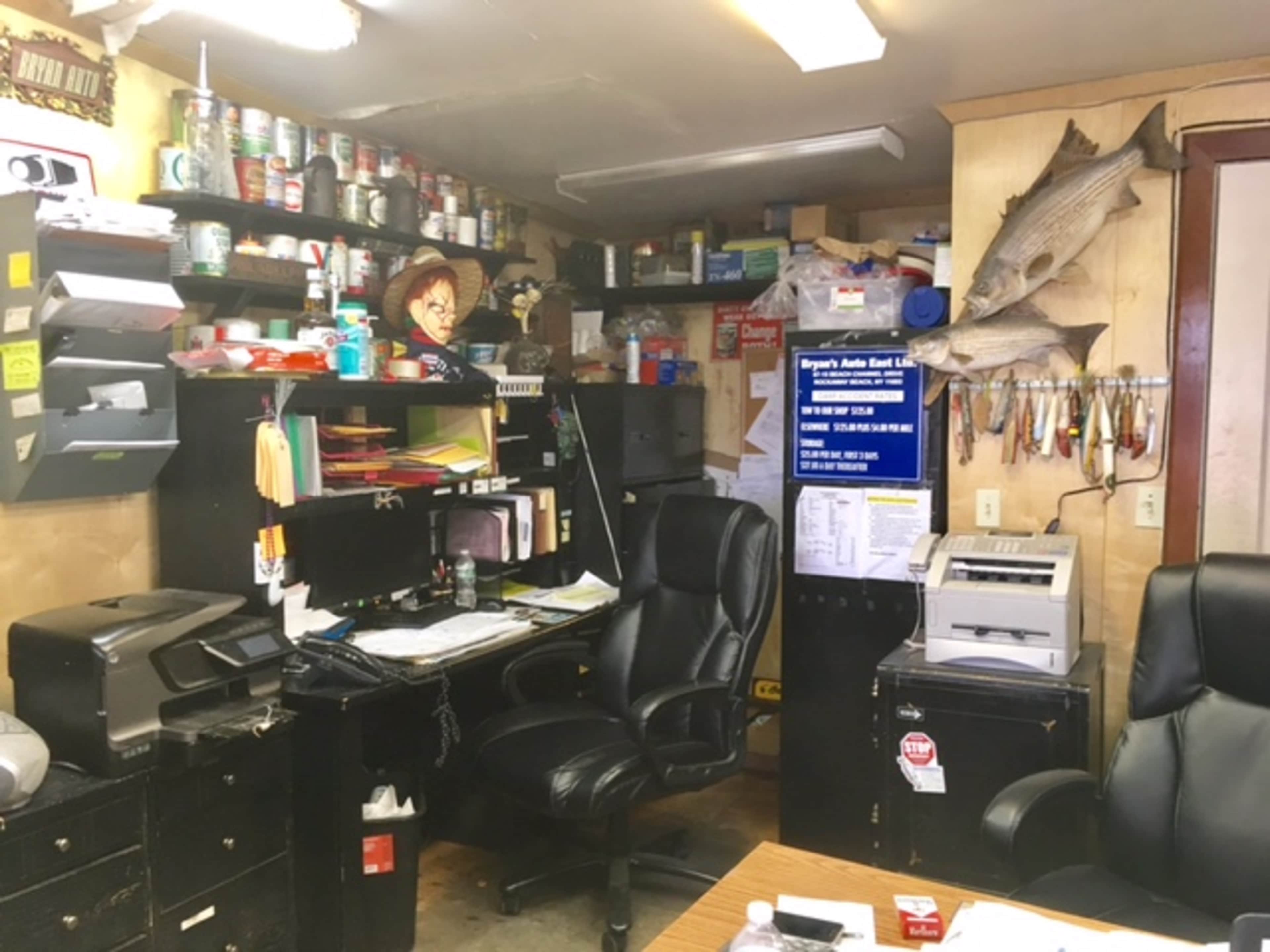 A cluttered office space with a black desk, filing cabinets, documents, and mounted fish on the wall.