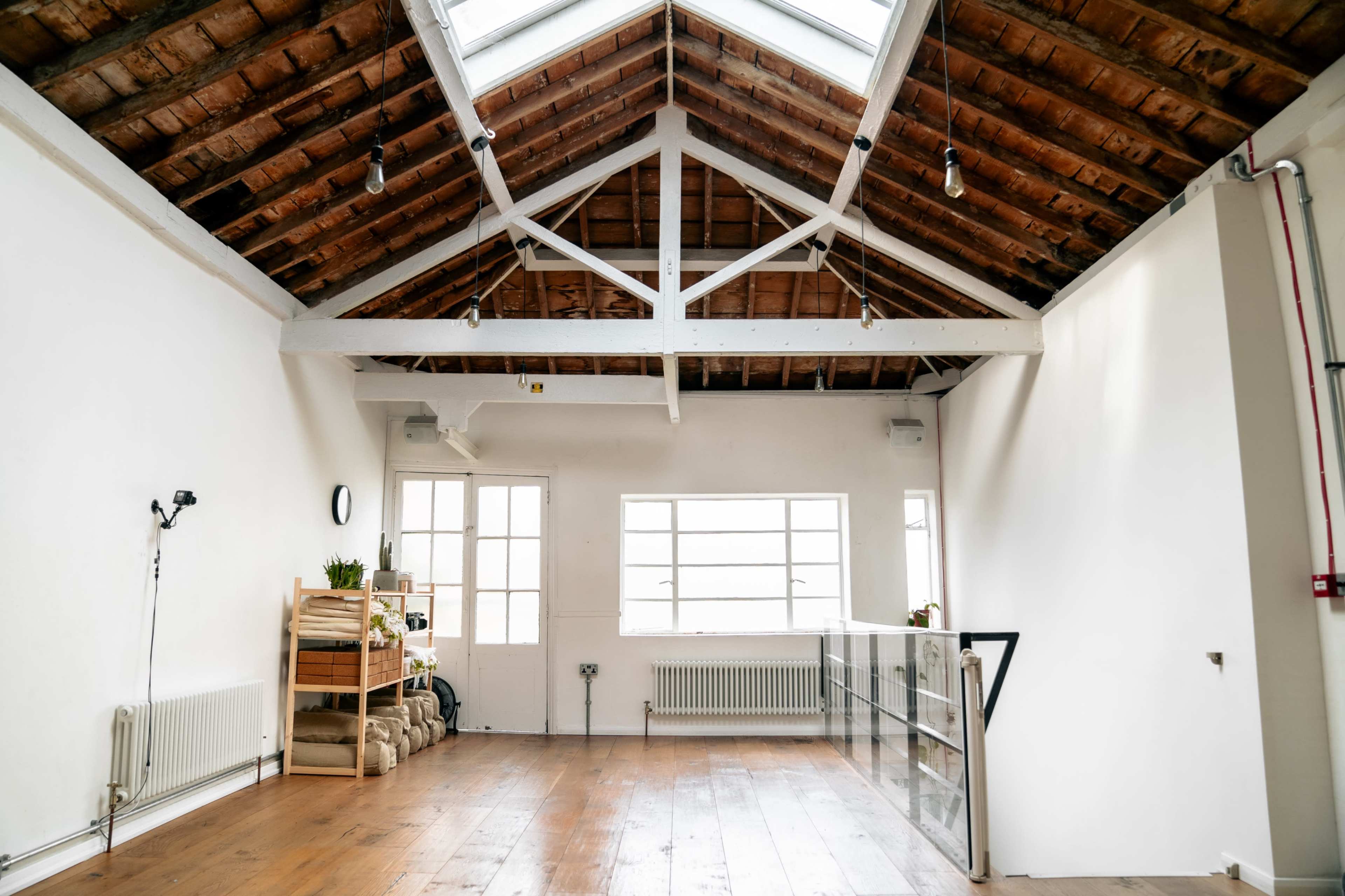 A spacious interior with a high, exposed beam ceiling, large windows, and wooden flooring, featuring minimal furnishings.