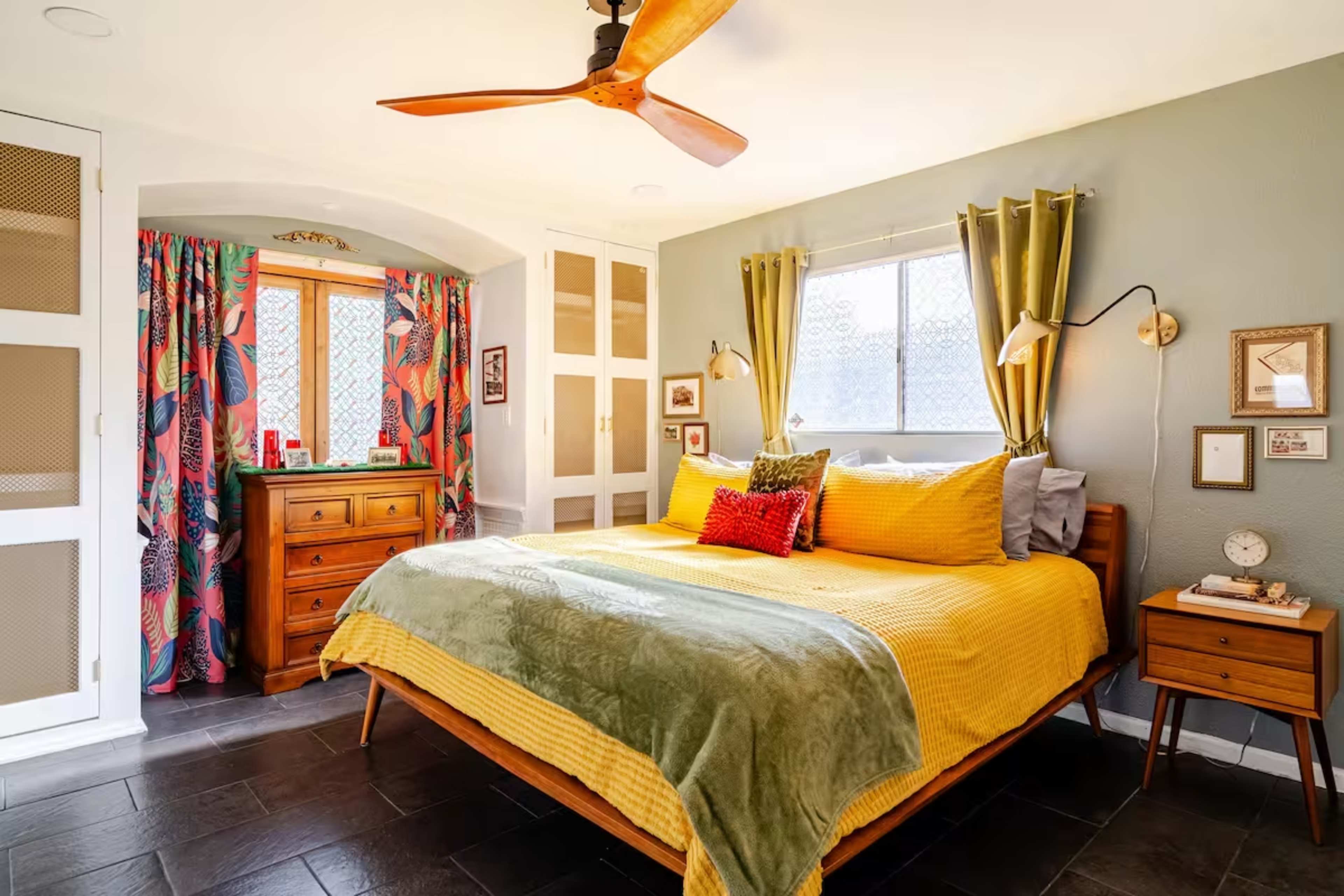 The image shows a brightly colored bedroom featuring a large yellow bed with green accents, a wooden dresser, and patterned curtains.