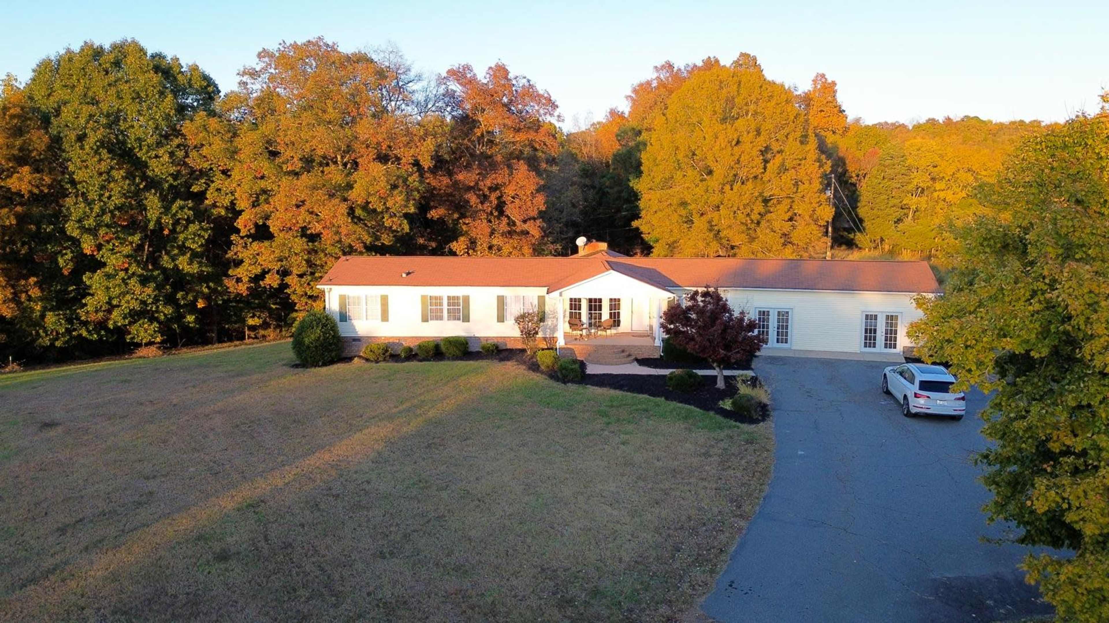 The image shows a single-story home situated on a grassy lot surrounded by trees with autumn foliage.