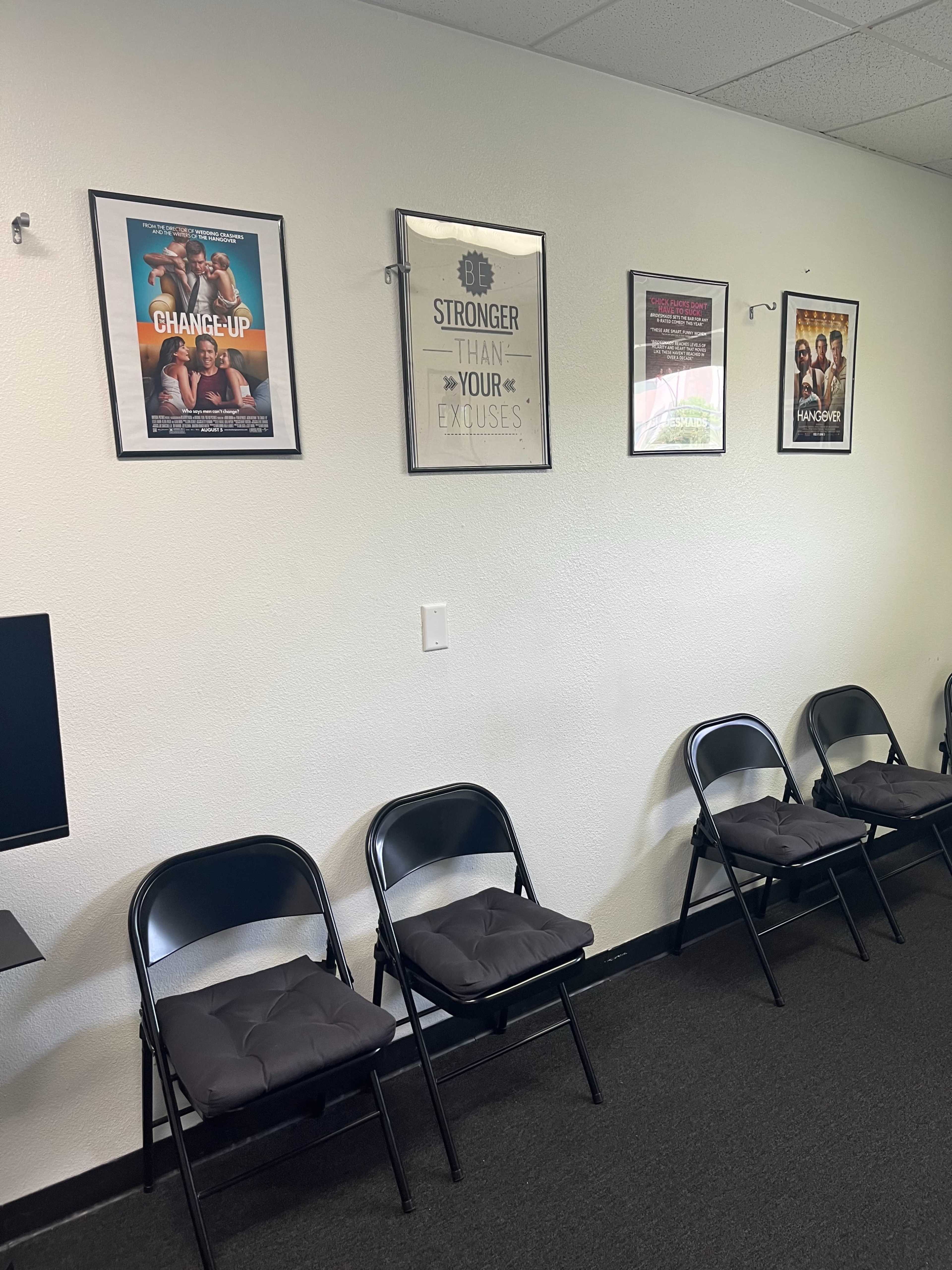 A wall with six framed movie posters and a row of black folding chairs arranged in front of it.