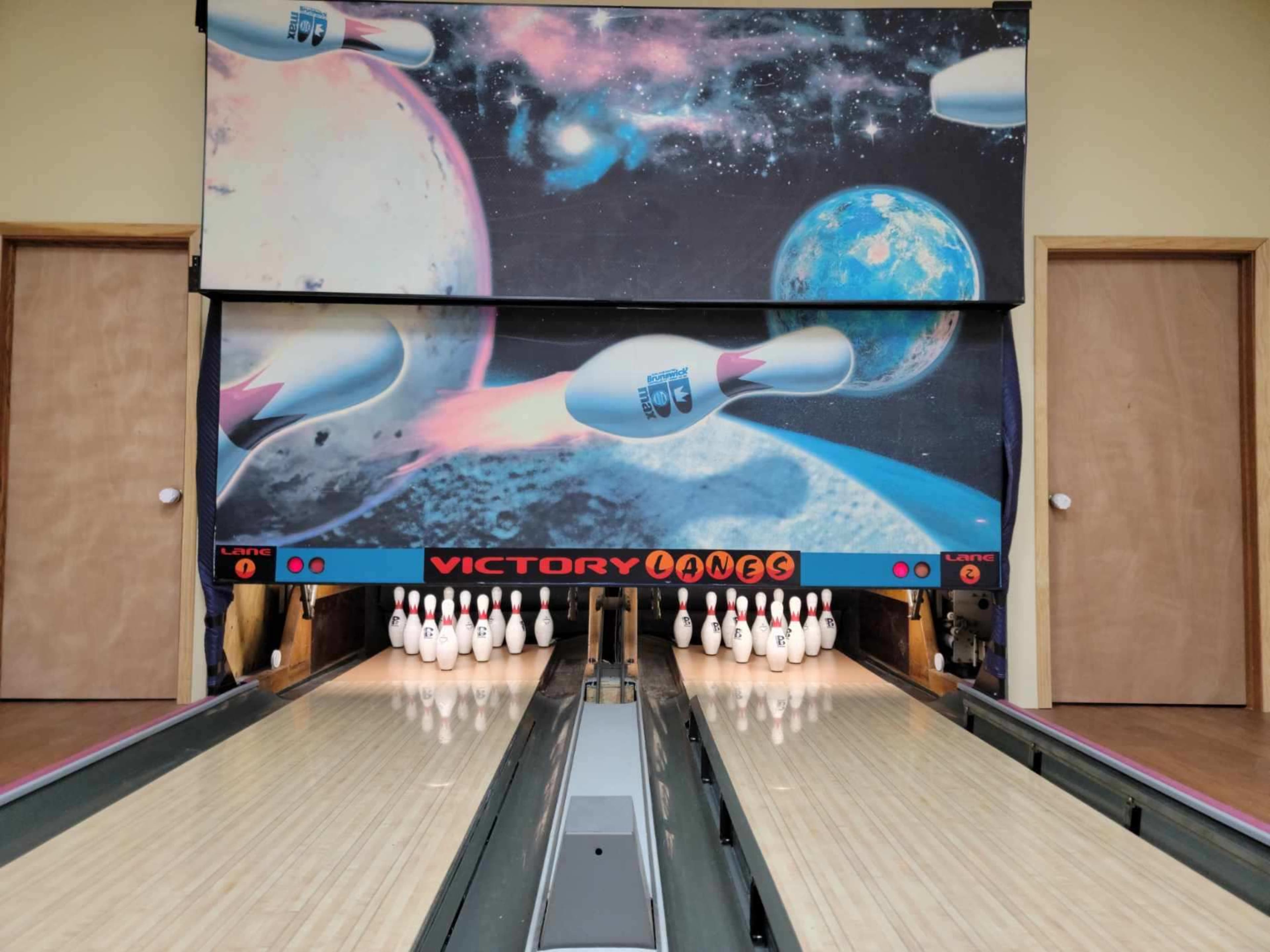 A bowling alley with a vibrant cosmic mural featuring planets and bowling pins set up for a game.