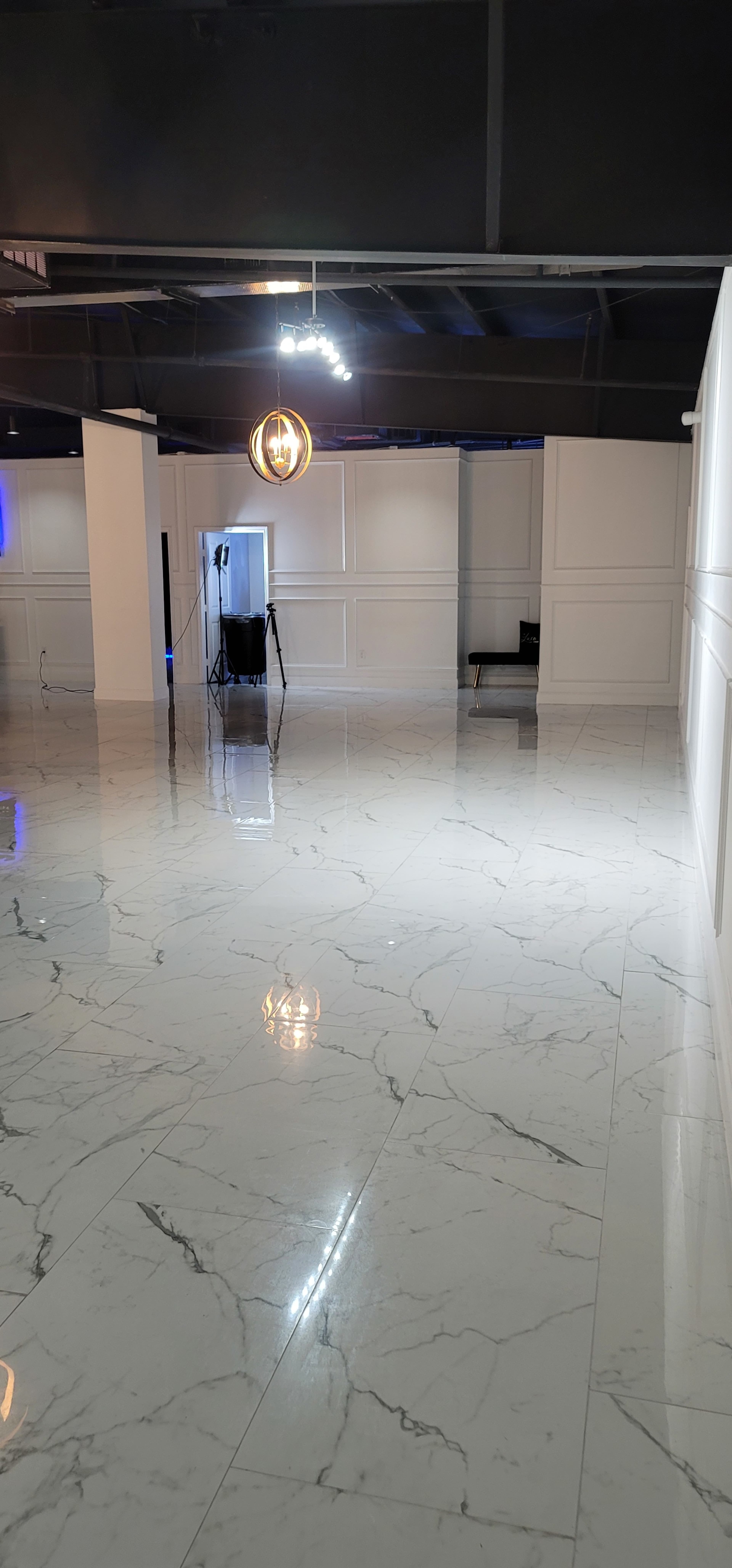 A spacious, empty room with polished marble flooring and white walls, illuminated by overhead lighting.