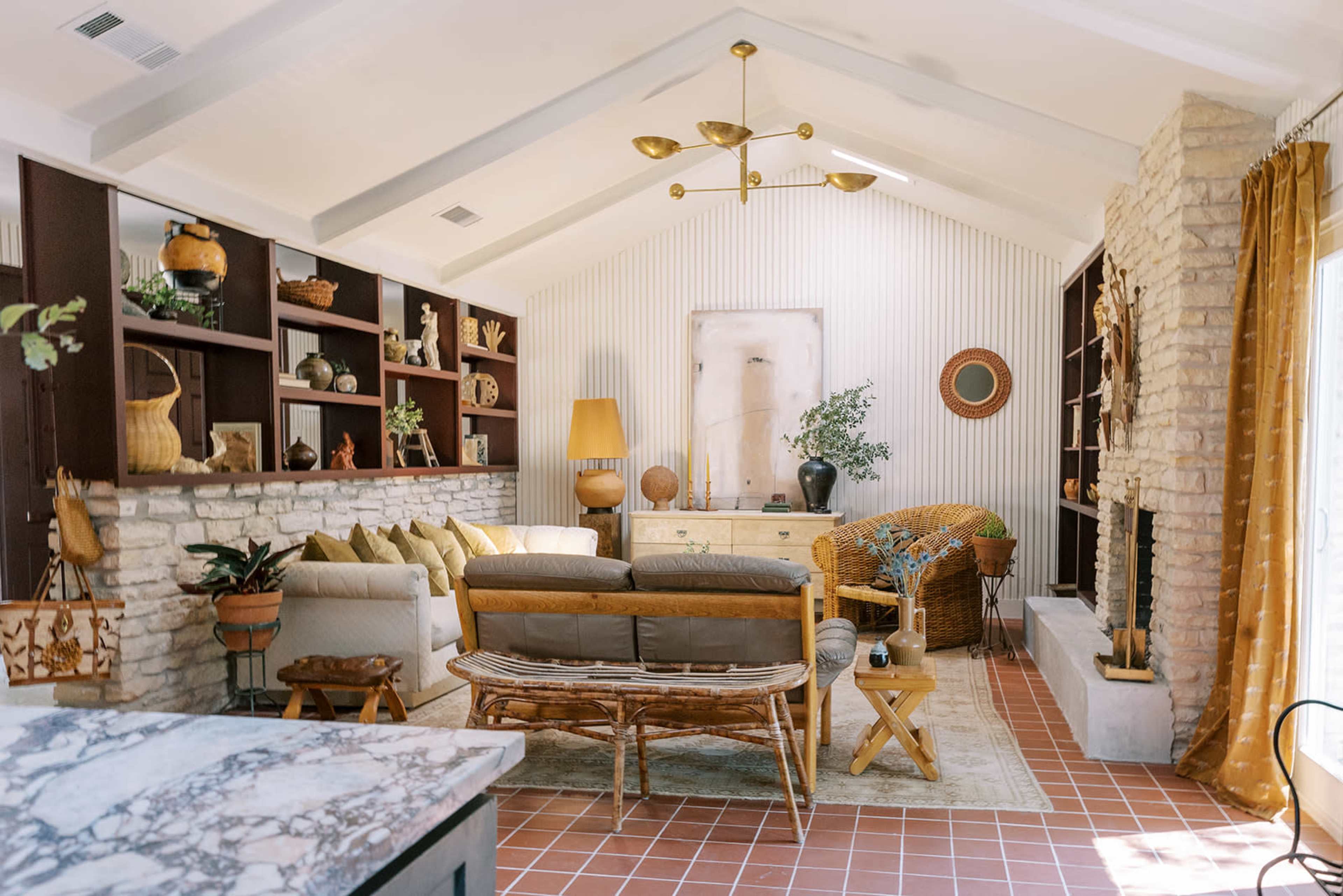 A well-decorated living room with a stone fireplace, a mix of furniture styles, and shelves adorned with decorative items.