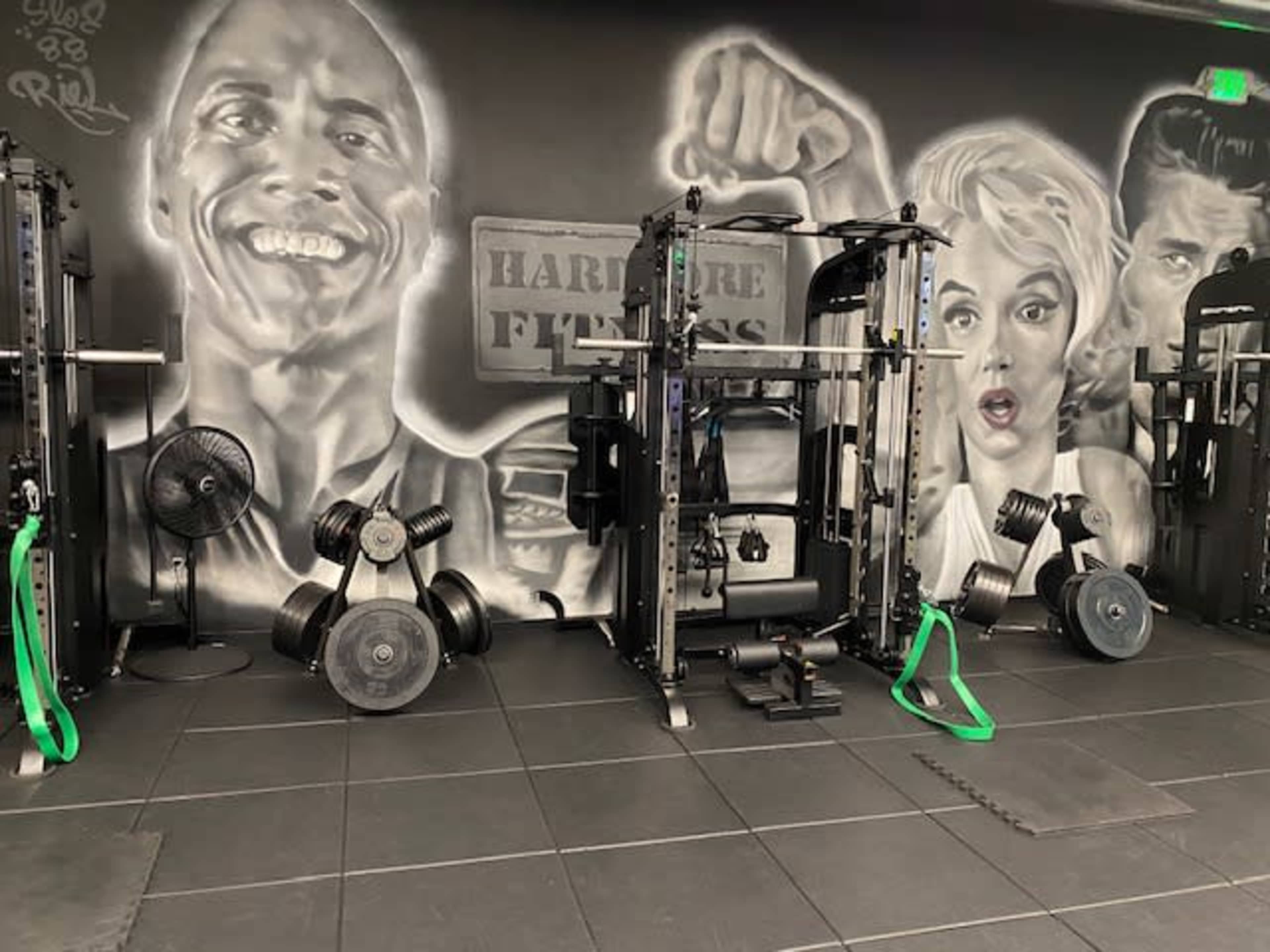 The image shows a fitness area with gym equipment set against a wall featuring large black-and-white portraits of iconic figures.