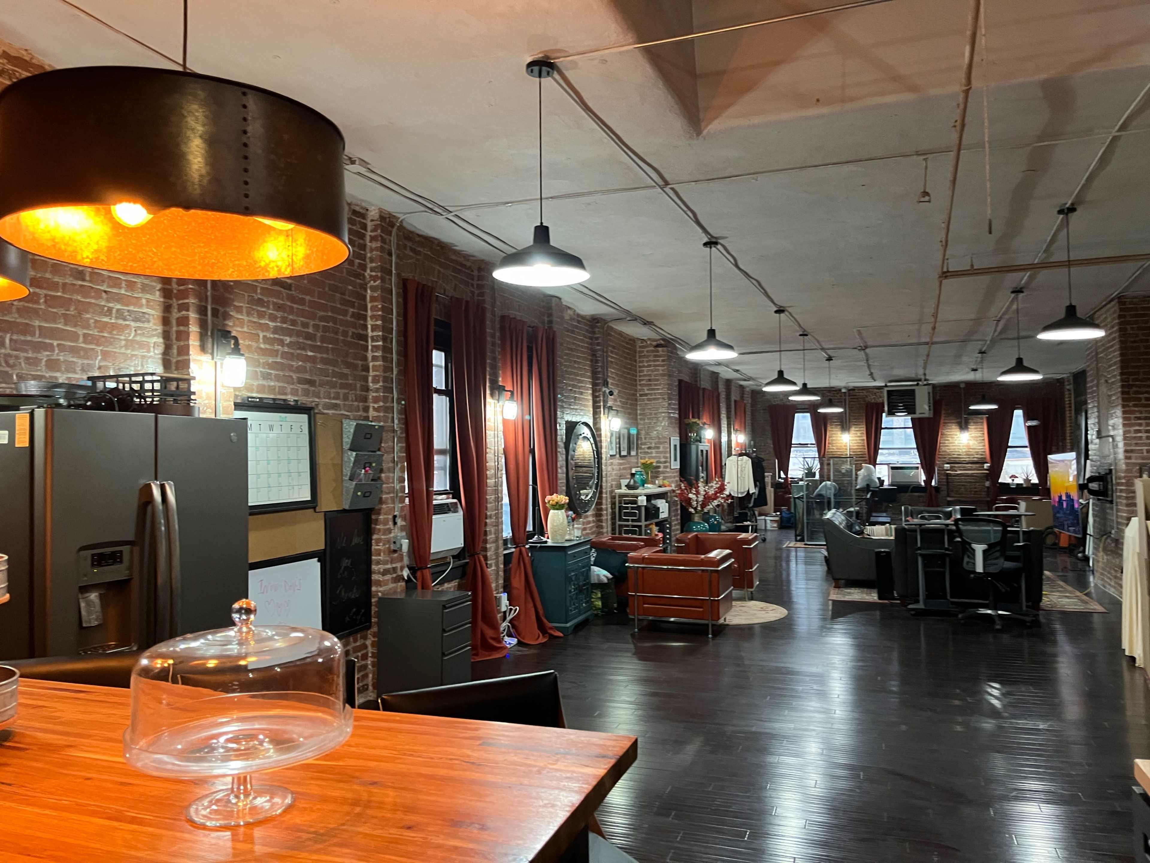 A spacious industrial-style loft with exposed brick walls, wooden flooring, and modern furniture, illuminated by hanging lights.