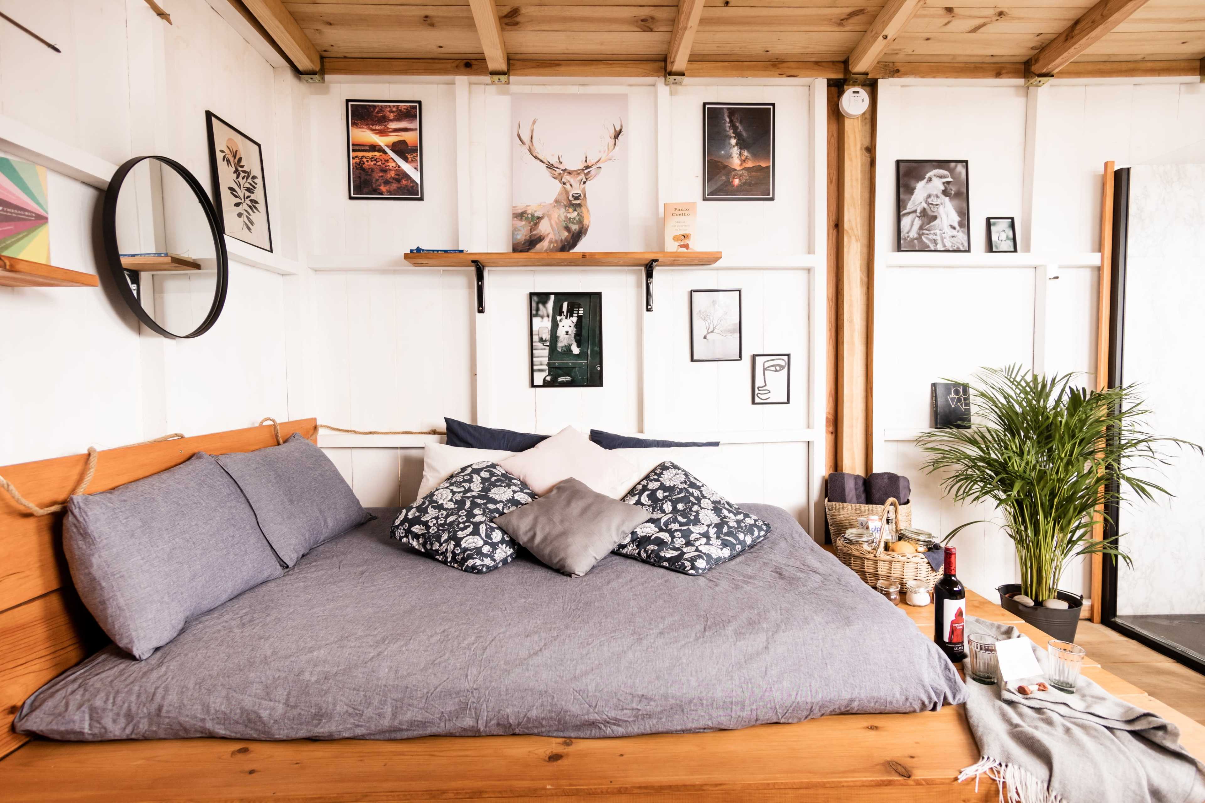 The room features a wooden bed with gray bedding, framed artwork on the walls, and a small plant in the corner.