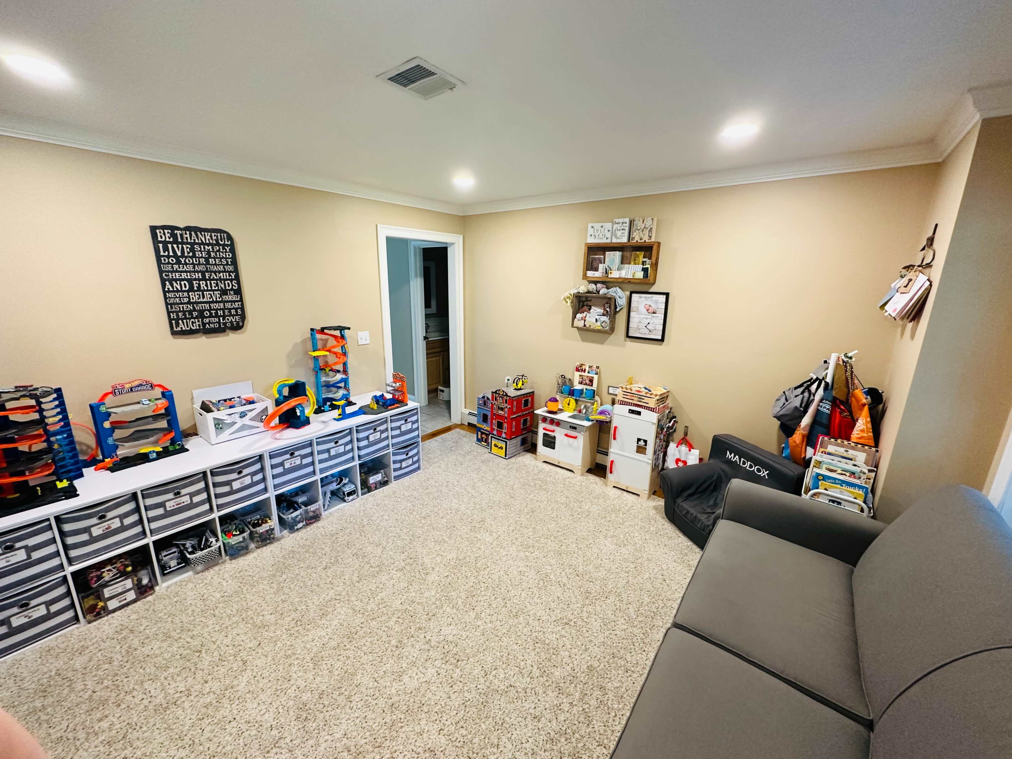 A playroom features organized storage containers filled with toys, a sofa, and wall-mounted shelves displaying various items.