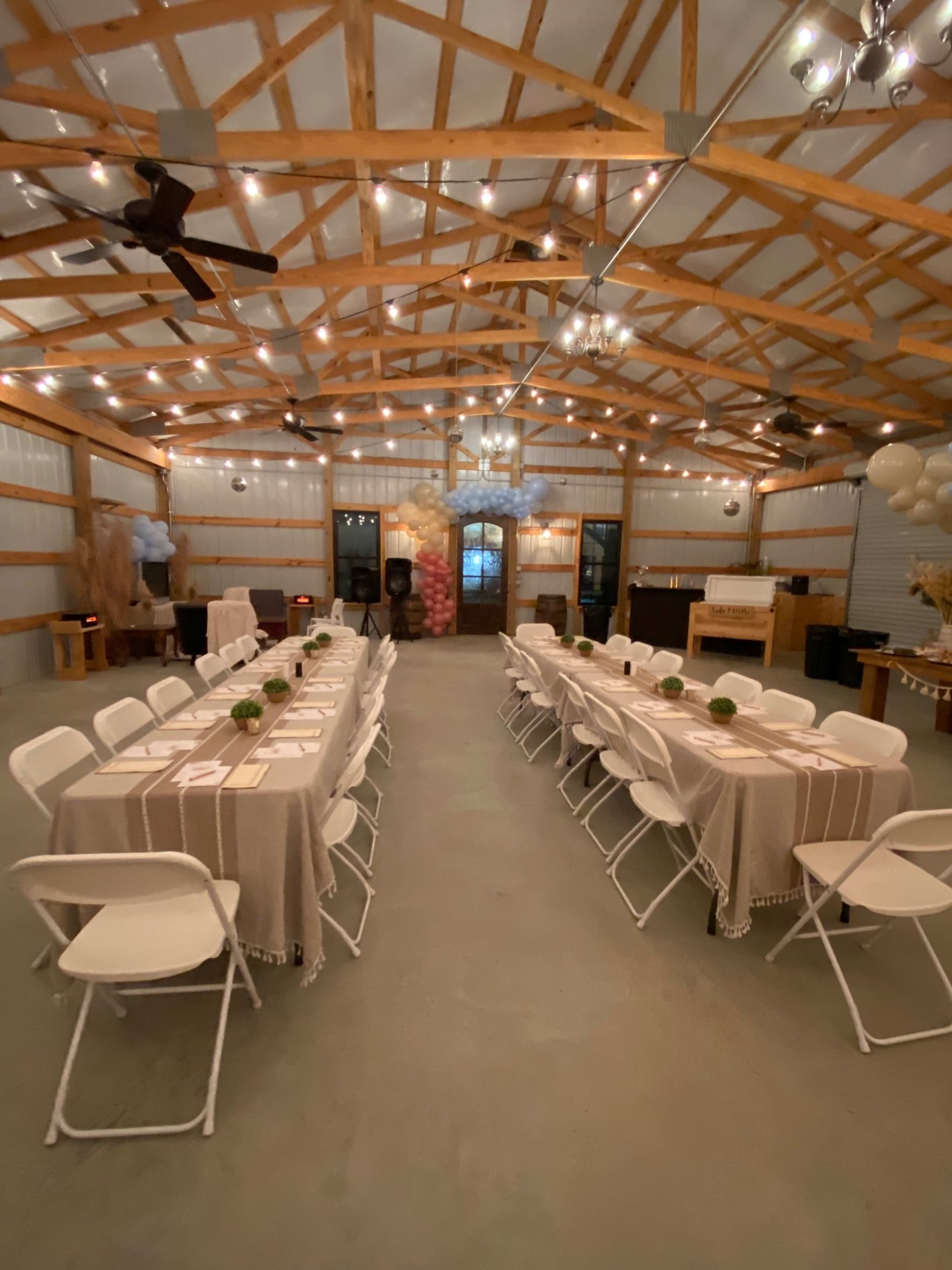 A banquet hall with two rows of tables set for an event, illuminated by string lights and featuring decorative elements along the sides.