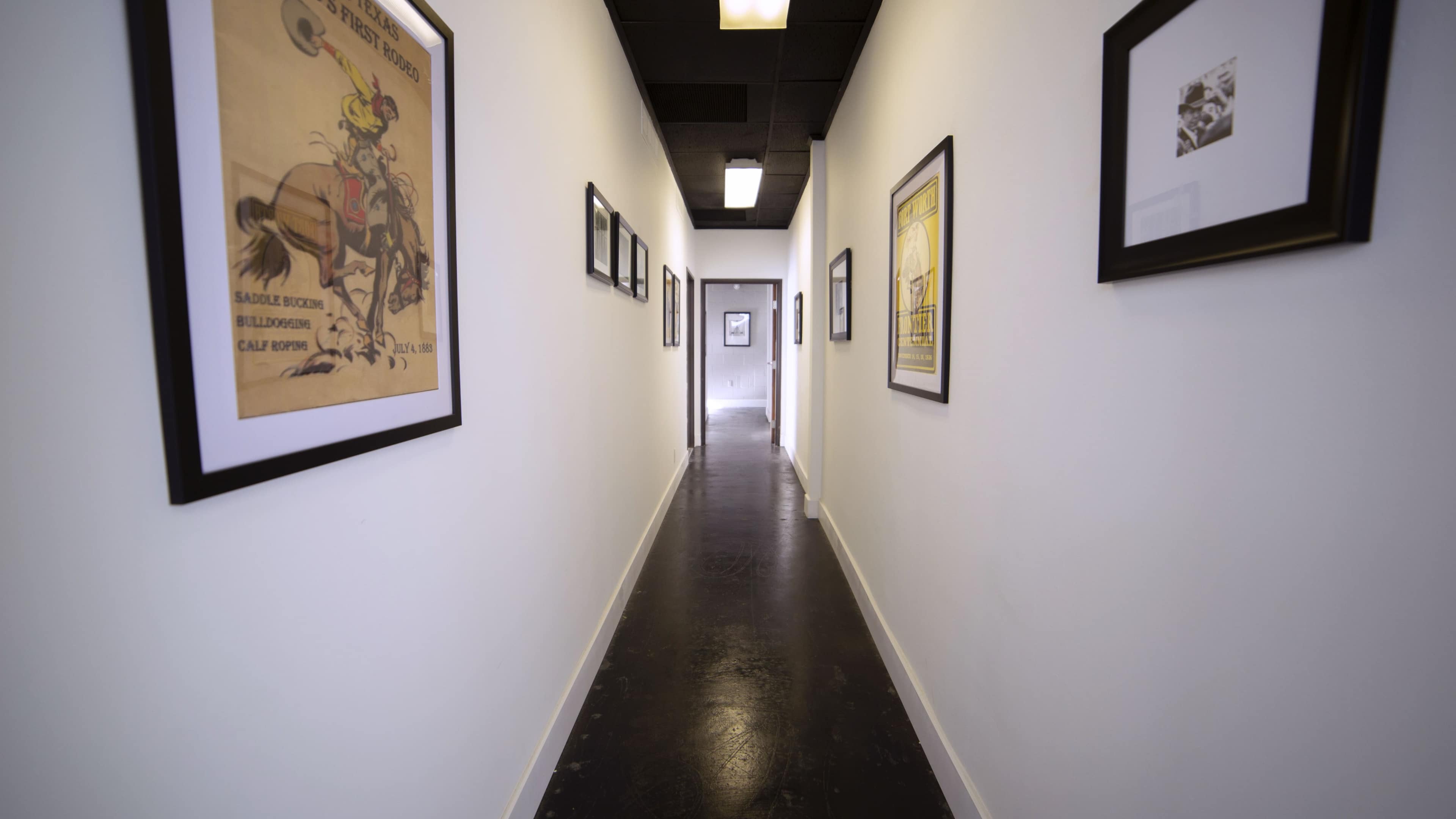 A long, narrow hallway with framed artwork on the walls and ceiling lights above.