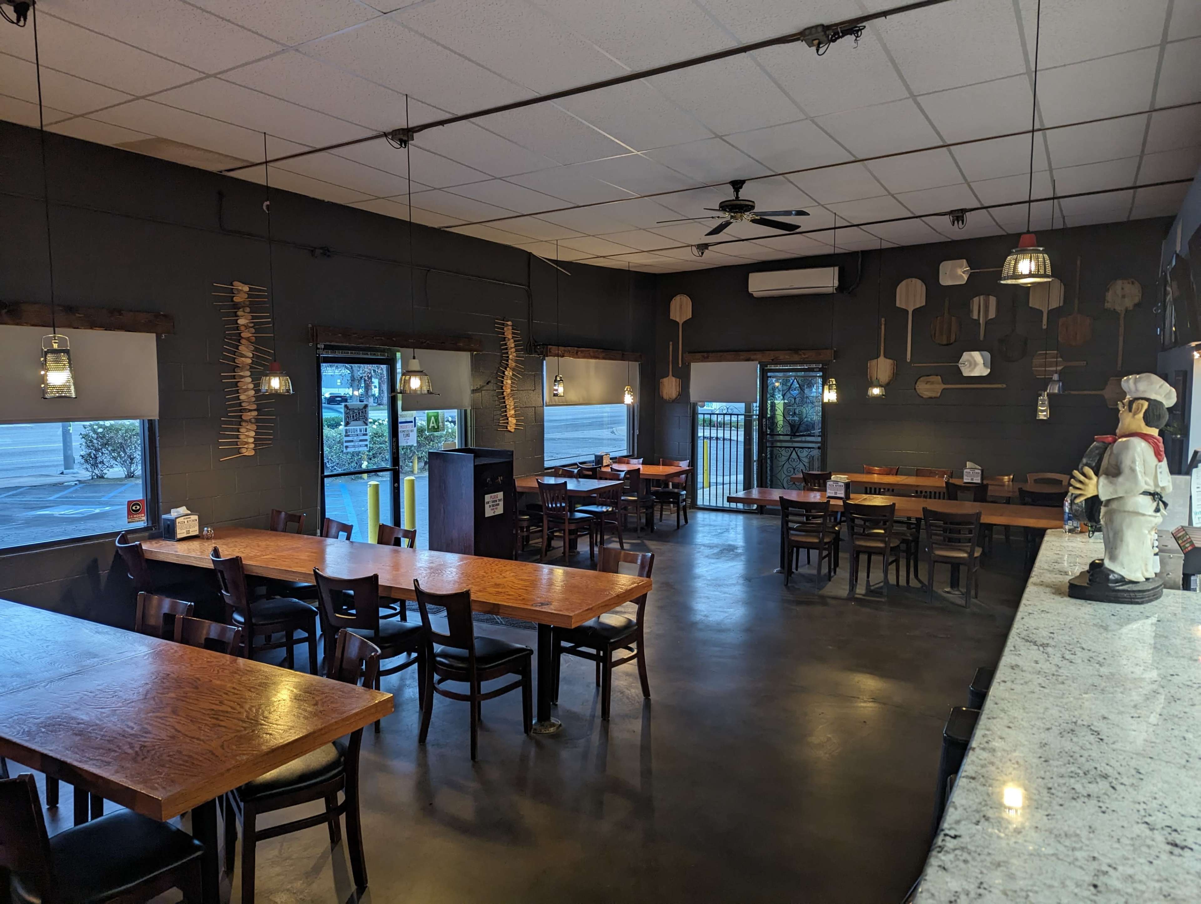A spacious restaurant interior with wooden tables and chairs, pendant lighting, and a granite countertop, featuring a chef figurine on the counter.
