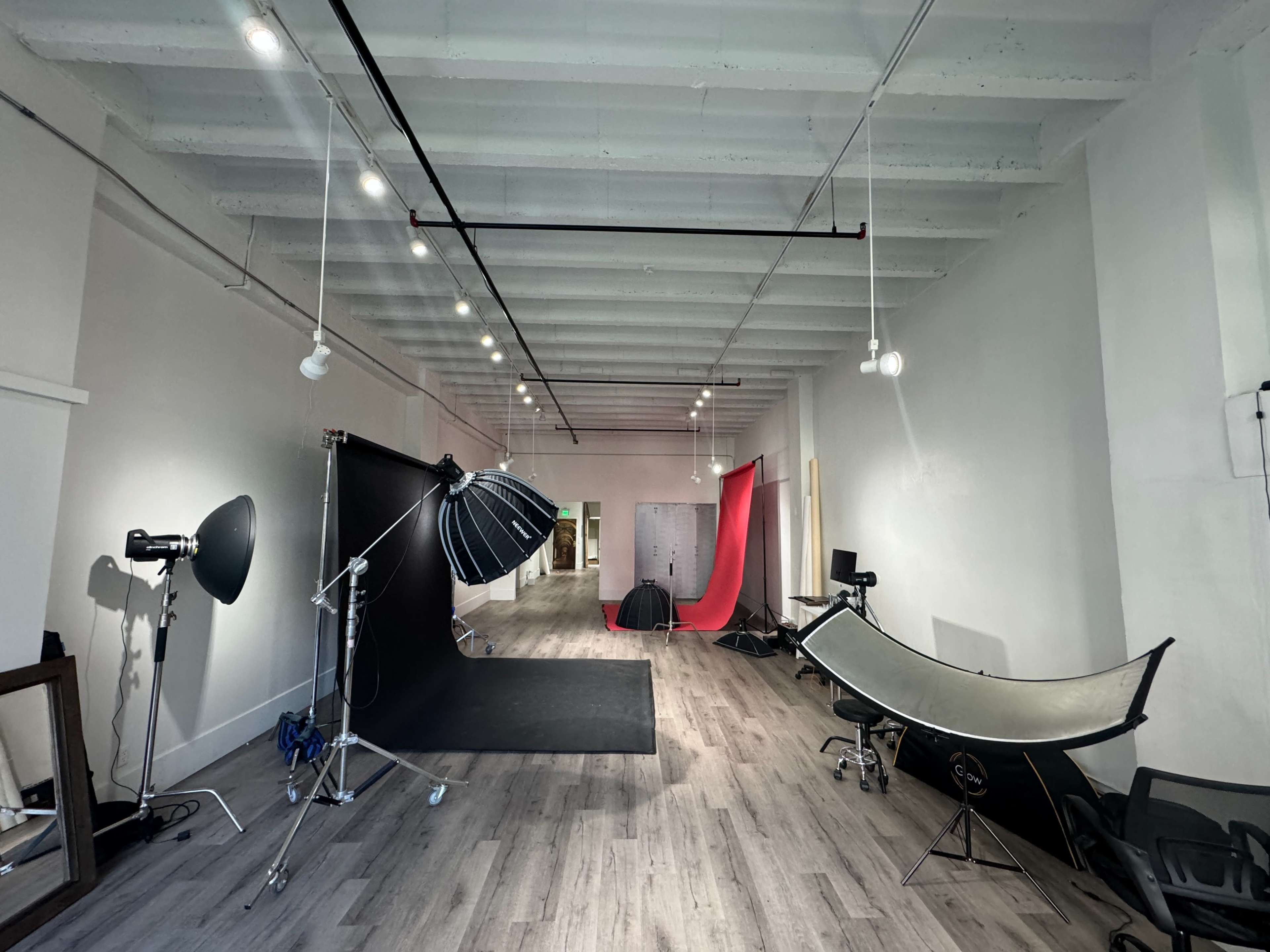 The image shows a spacious photography studio with various backdrop setups, lighting equipment, and a wooden floor.