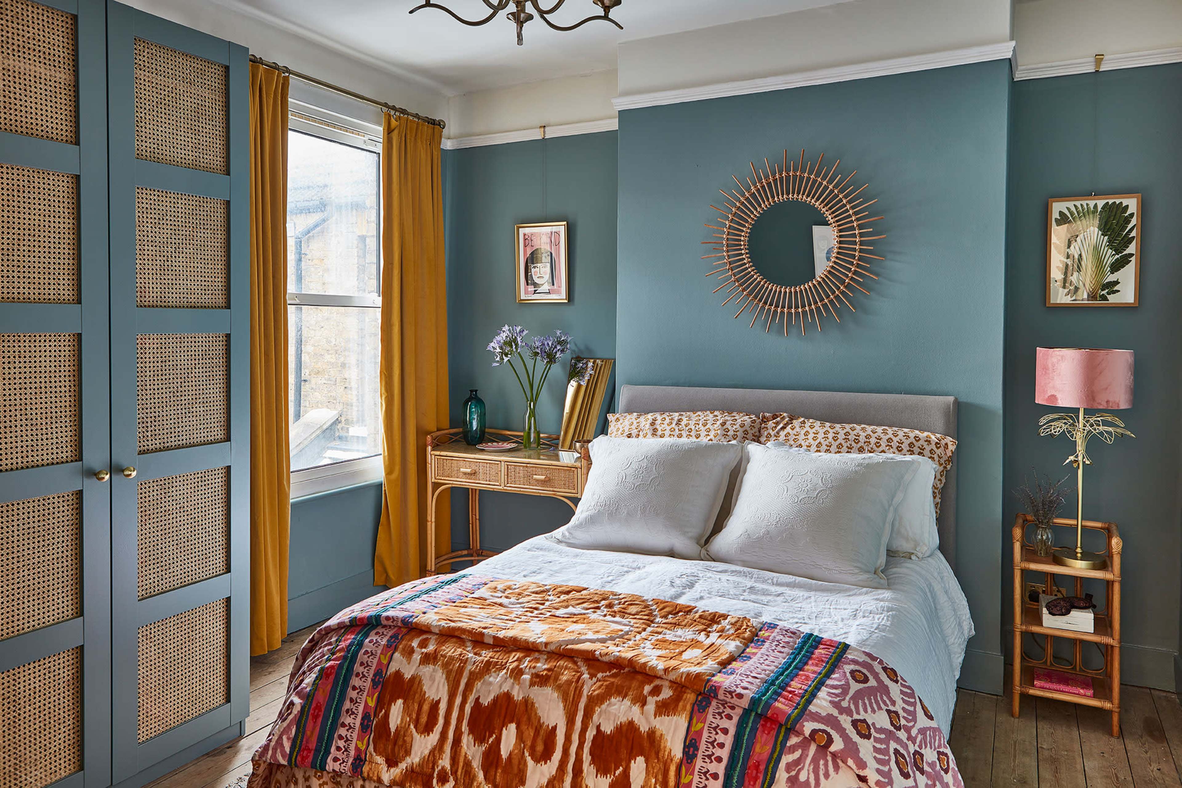 A cozy bedroom featuring a bed with patterned bedding, a wooden desk, and a window with yellow curtains.