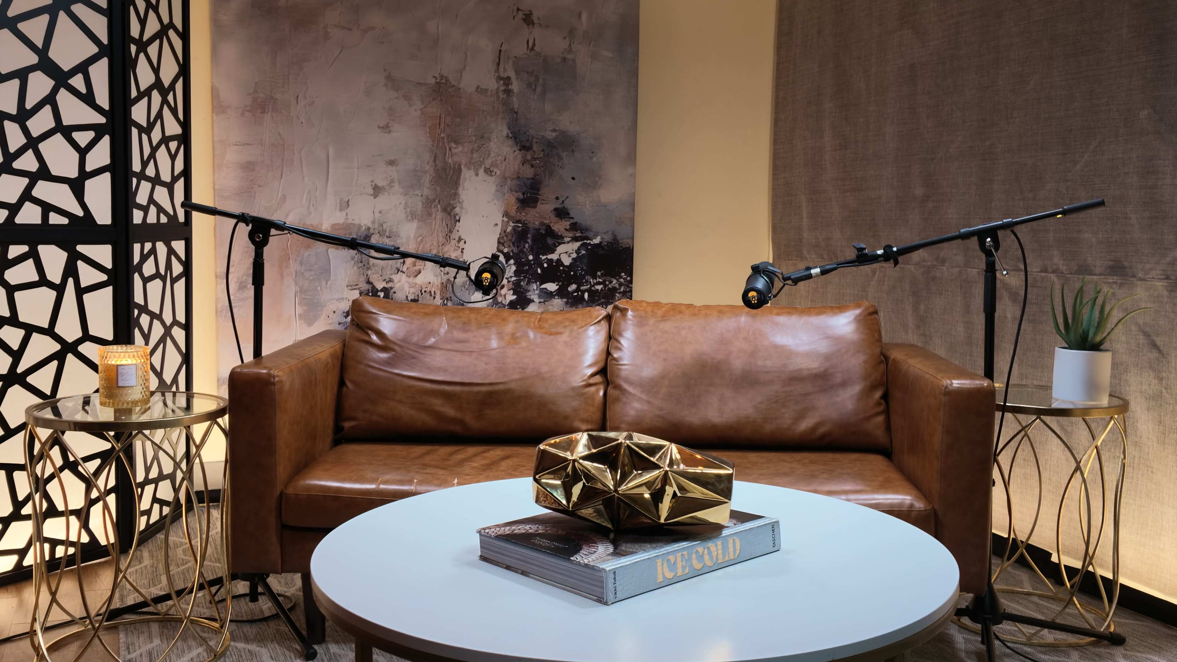 The image shows a modern living space featuring a brown leather sofa, a round white coffee table with decorative items, and two adjustable studio lights positioned on either side.