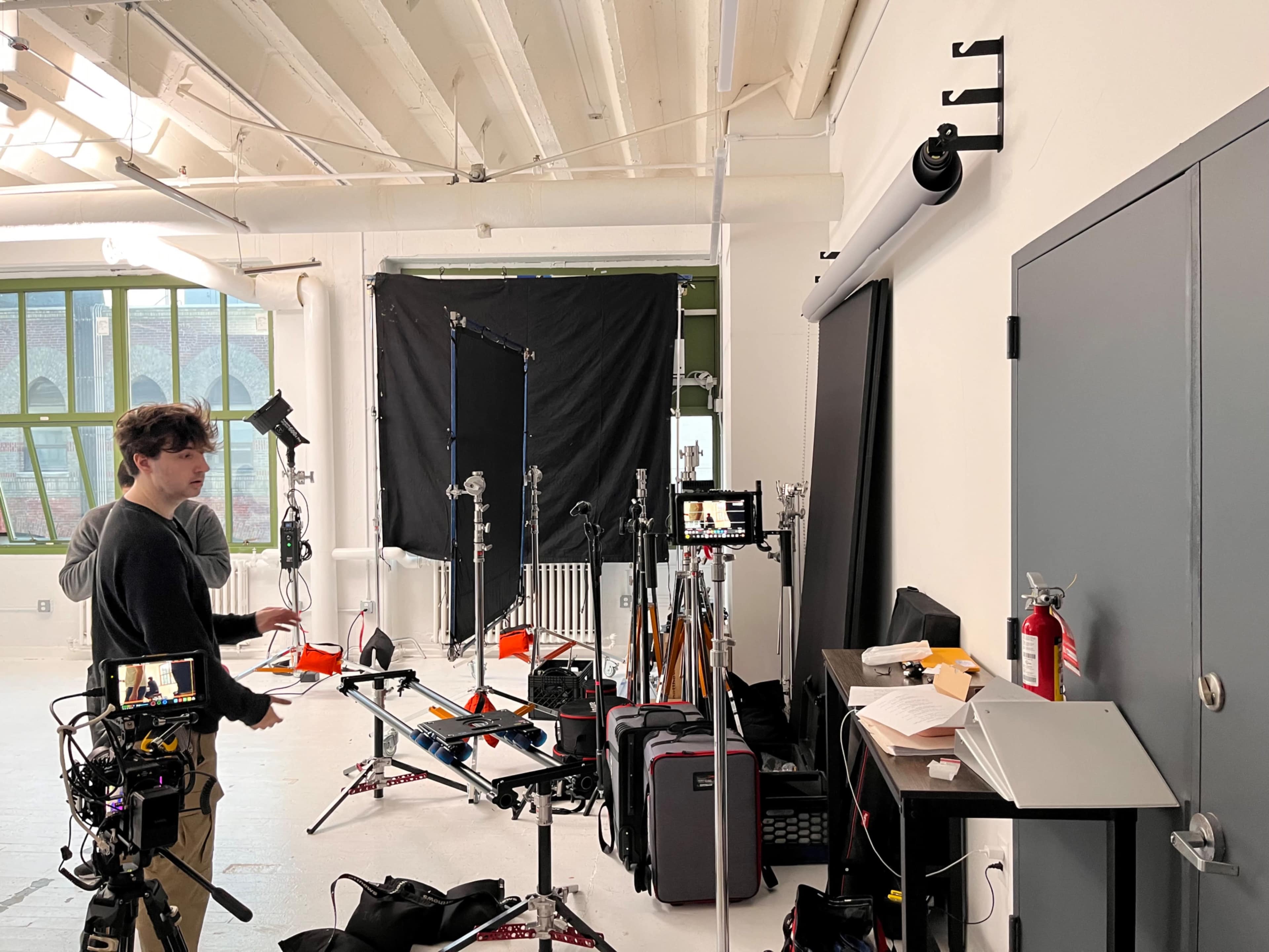 A person is setting up equipment in a studio featuring various lighting and camera gear along with a backdrop.