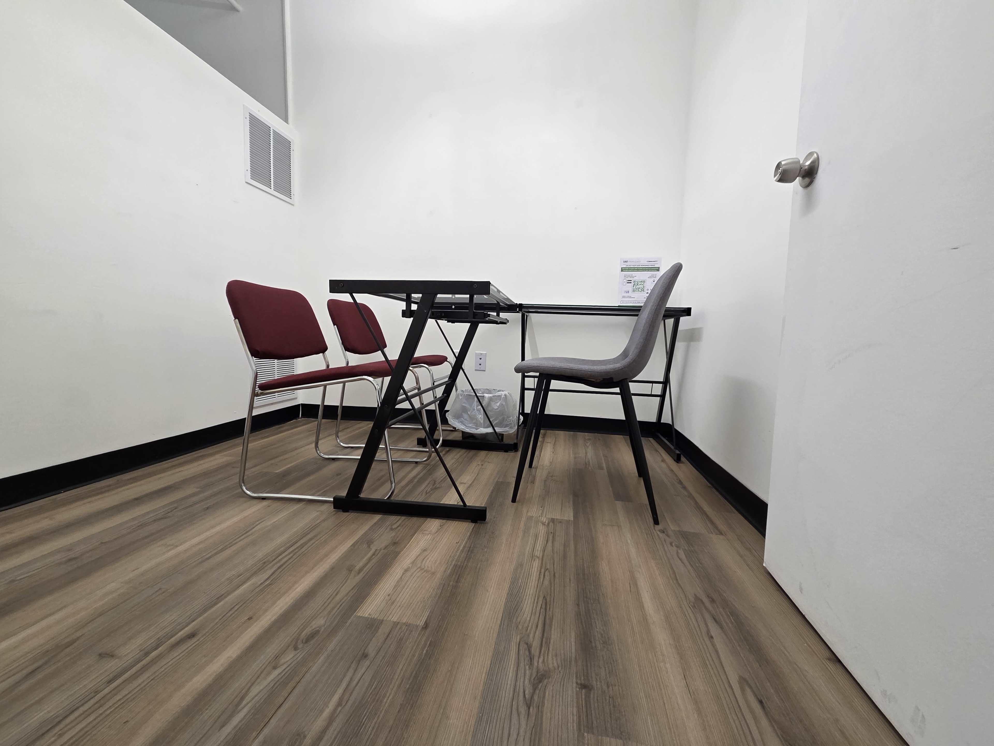 The image shows a small room with a table, four chairs, and a wastebasket on a wooden floor.