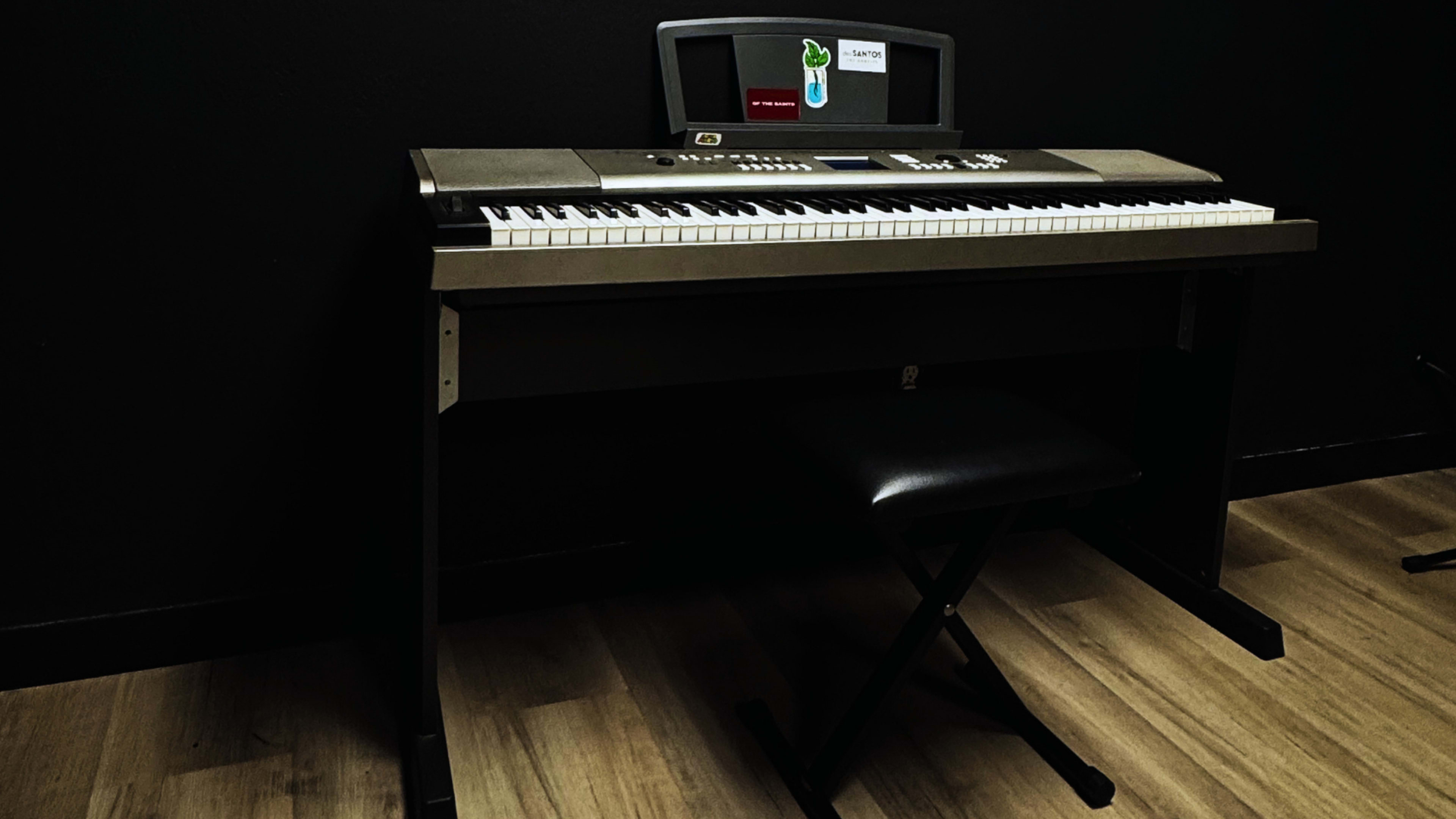 A digital piano sits on a black platform next to a single stool on a wooden floor.