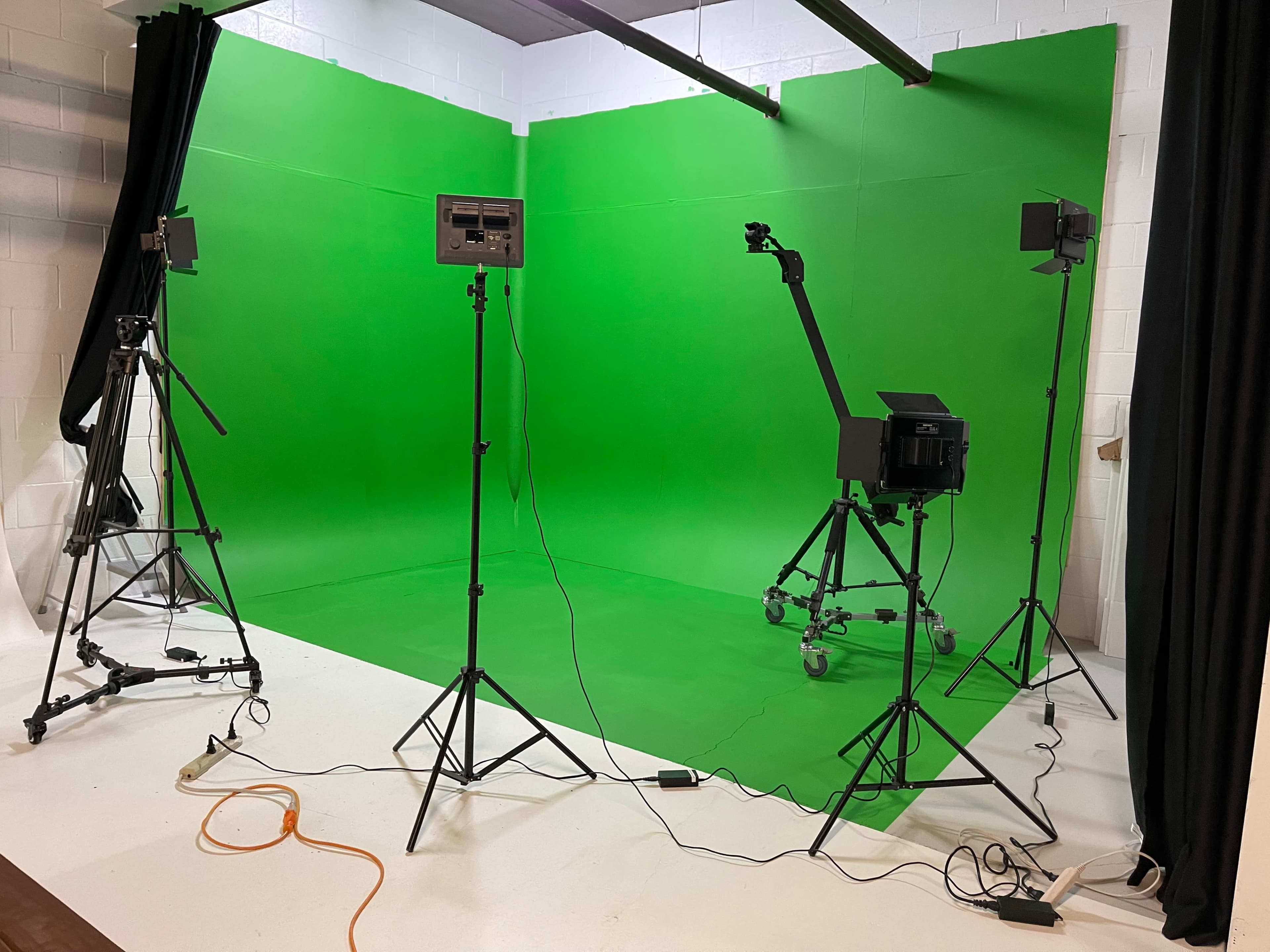 A studio setup with a green screen background, multiple lighting stands, and various equipment arranged on a white floor.